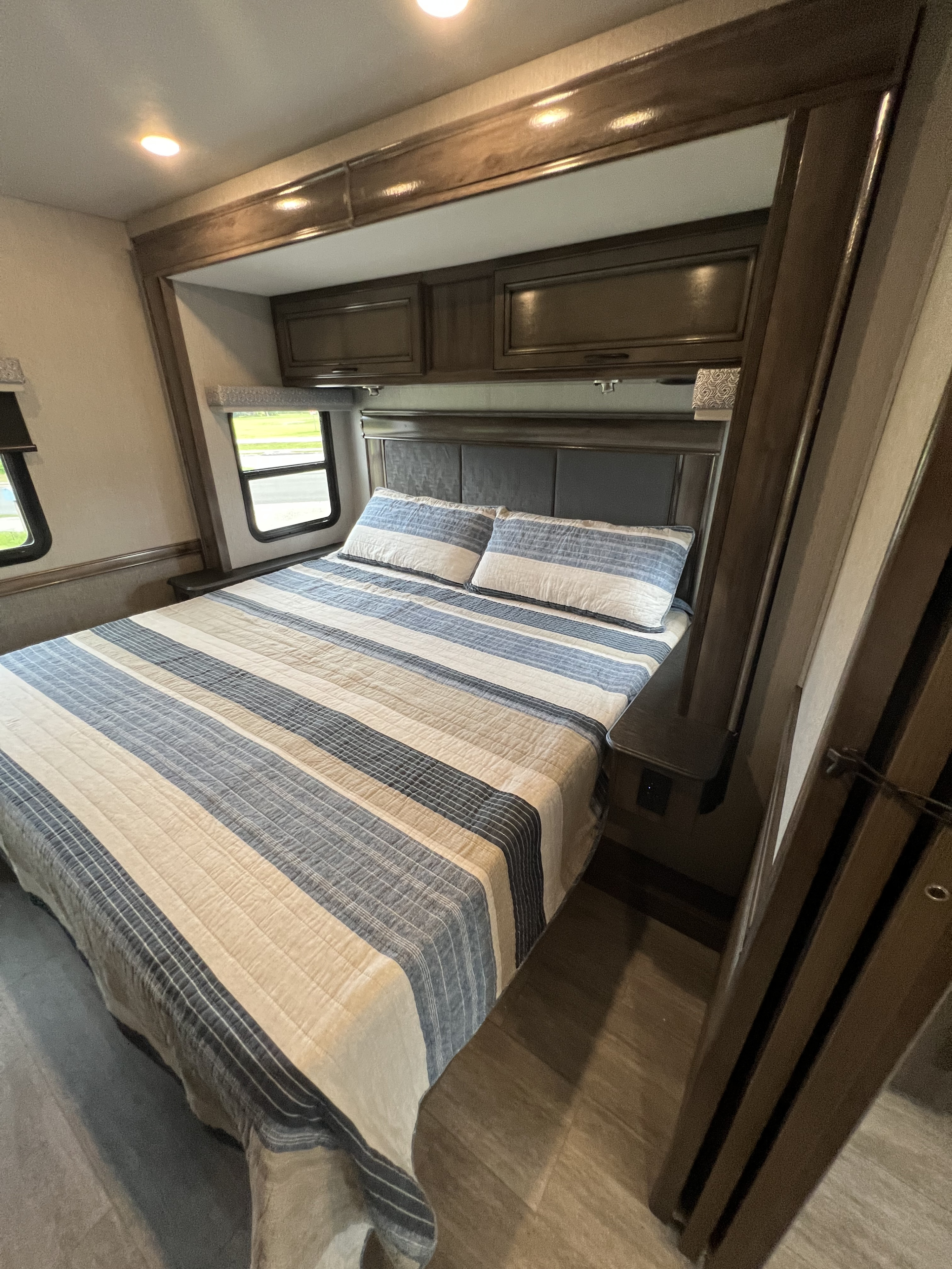 Cozy RV rental bedroom with striped bedding, built-in cabinets, and window views. Perfect for your next adventure.. Holiday Rambler Admiral 2023