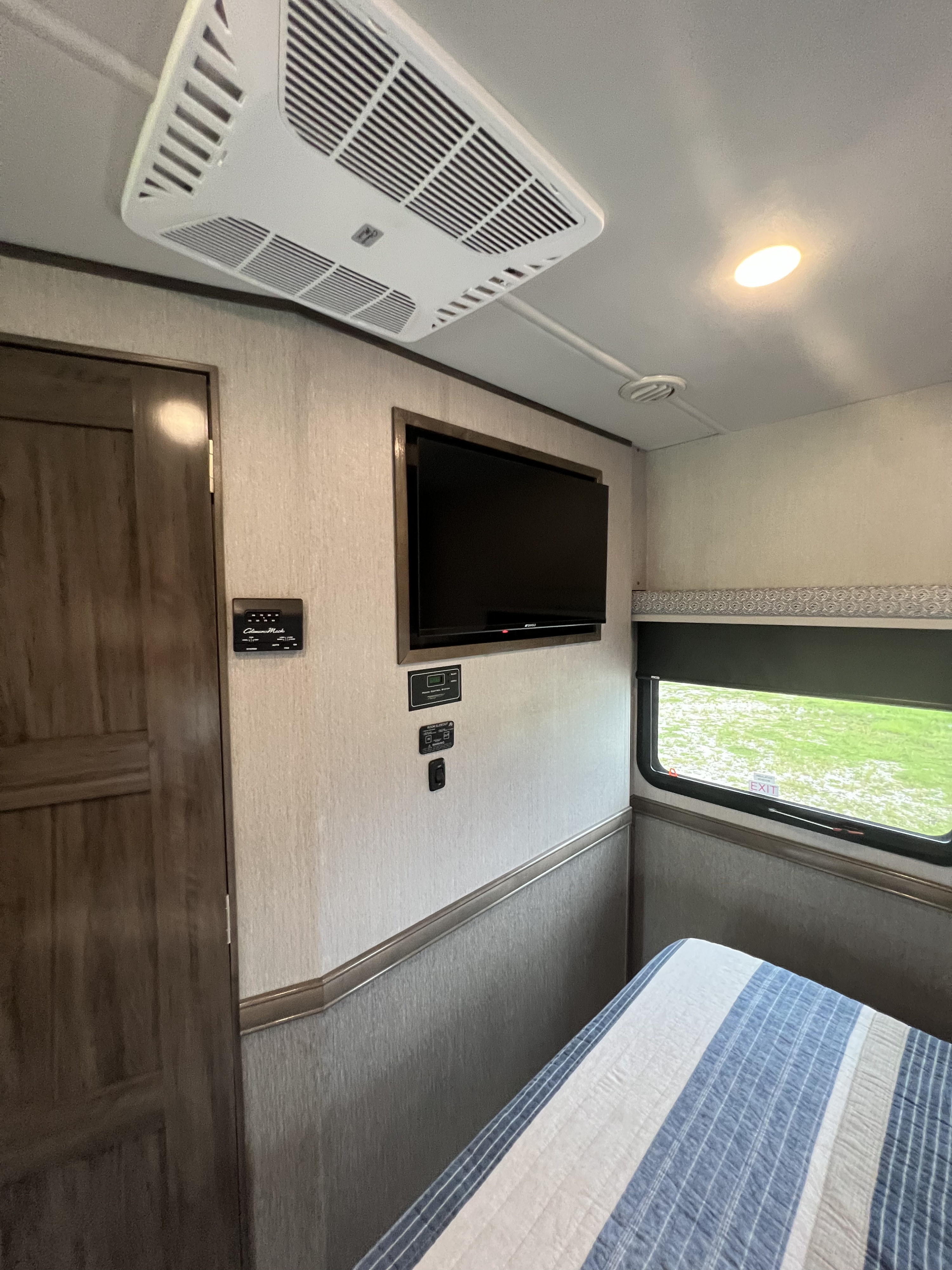 Experience comfort in this **rv rental** bedroom with a striped bed, wall-mounted TV, and overhead AC. Window offers outdoor views.. Holiday Rambler Admiral 2023