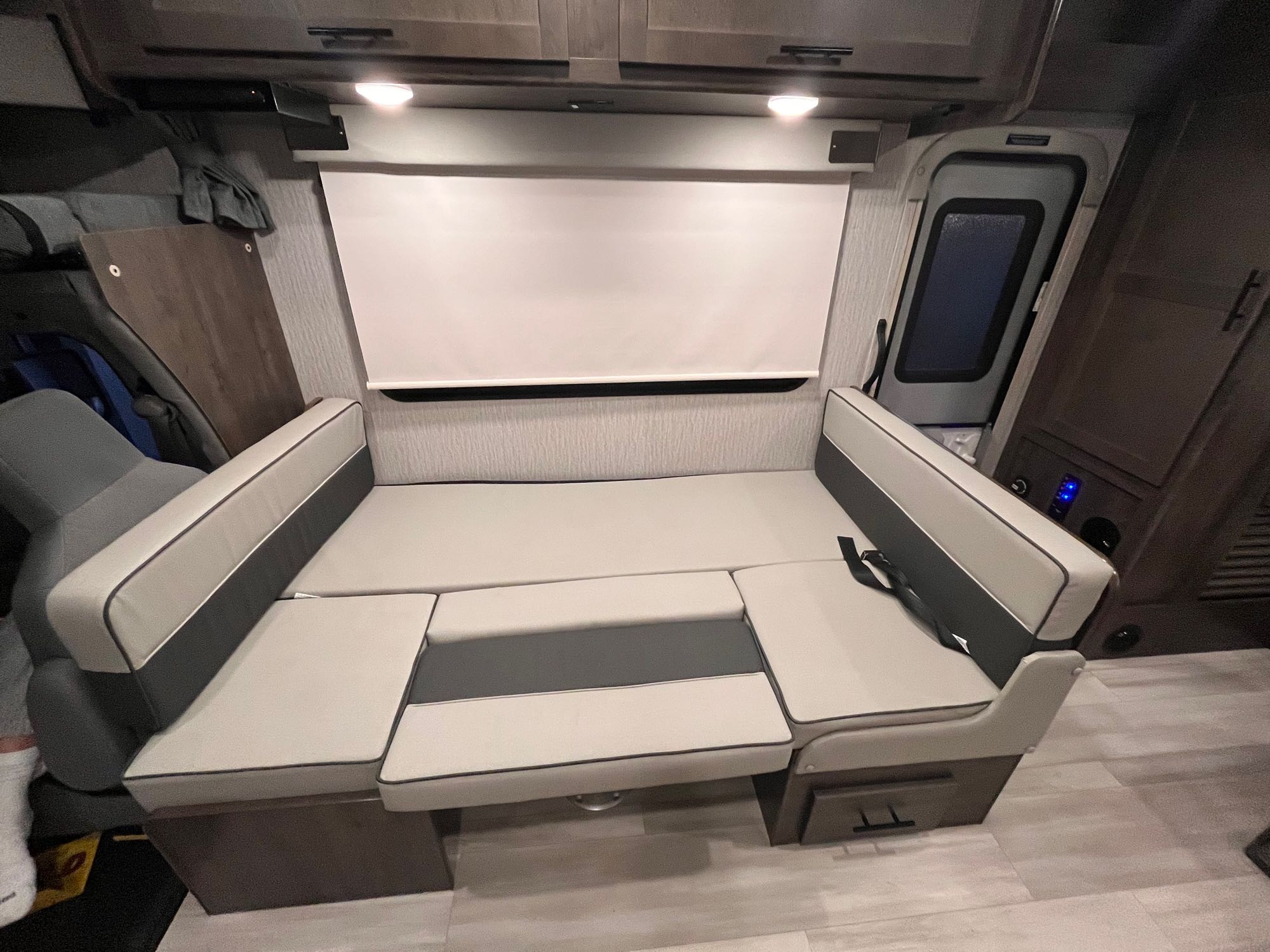 RV rental interior: Convertible dinette transforms into a sleeping area, featuring light-toned cushions and overhead storage.. Forest River Coachmen Leprechaun Premier 2022