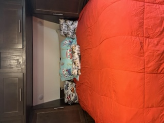 RV rental bedroom: A comfy bed with a red comforter, dark cabinets, and folded bedding in the bunk. Ready for travel adventures!. Forest River Cherokee Wolf Pup 2019