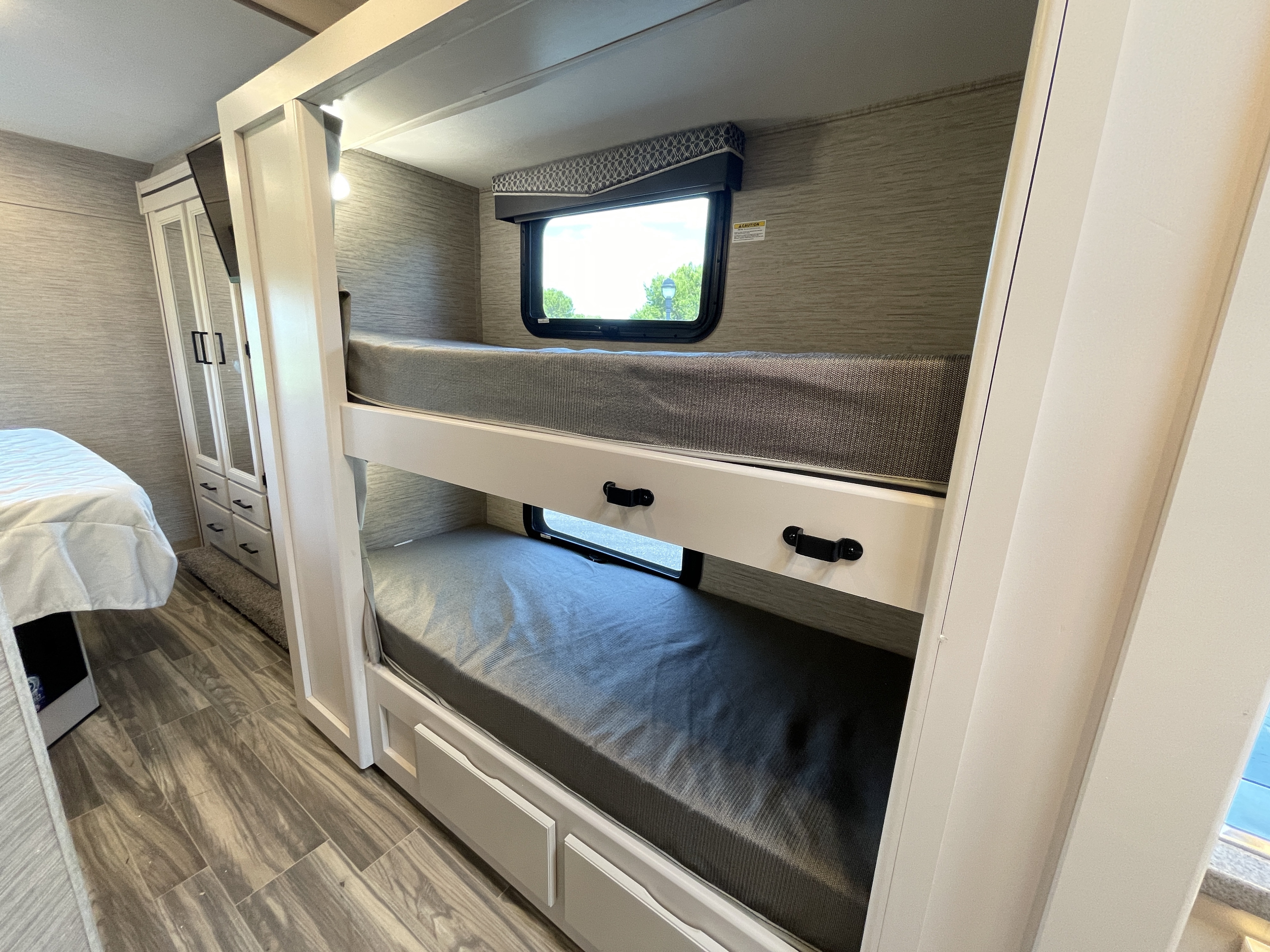 RV rental interior features bright, modern bunk beds with windows, grey mattresses, and a nearby wardrobe.. Thor Motor Coach Four Winds 2023
