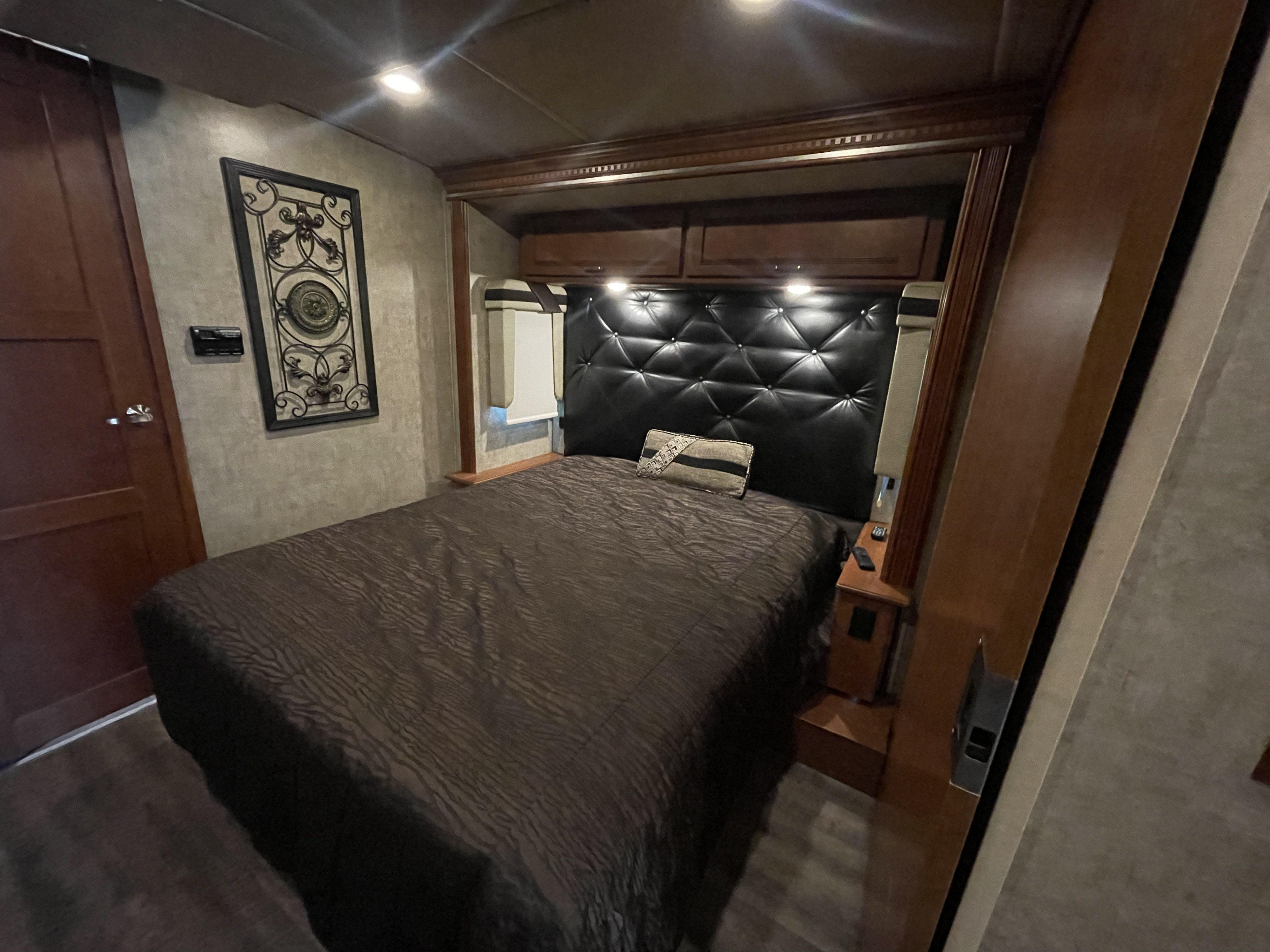 Cozy RV rental bedroom featuring a dark, patterned comforter, black tufted headboard, and warm wood cabinetry.. Itasca Solei 2015