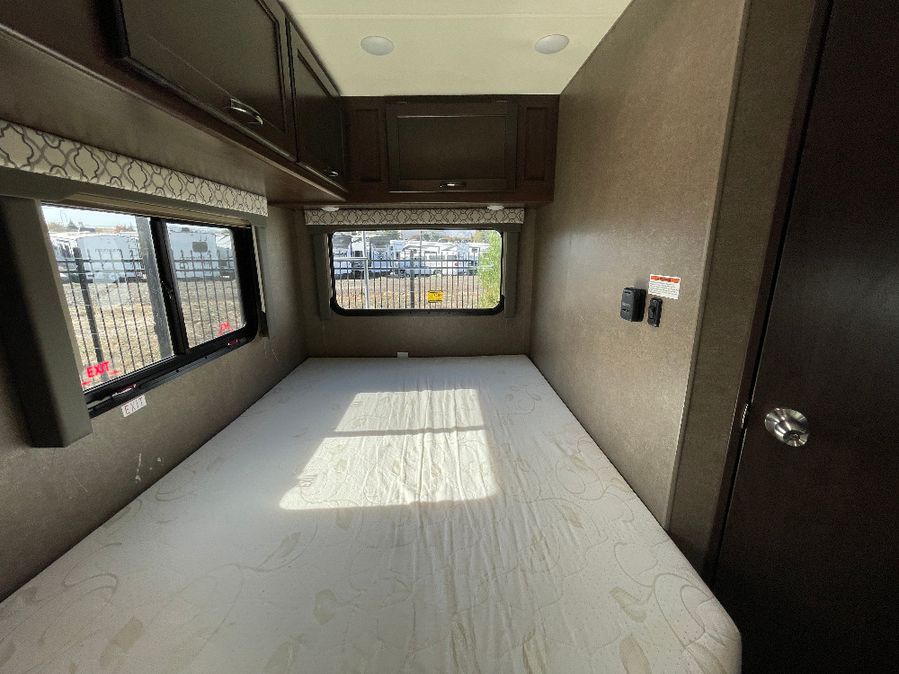 Spacious RV rental bedroom featuring a comfortable mattress, overhead cabinets, and windows with outdoor views.. Thor Freedom Elite 2019
