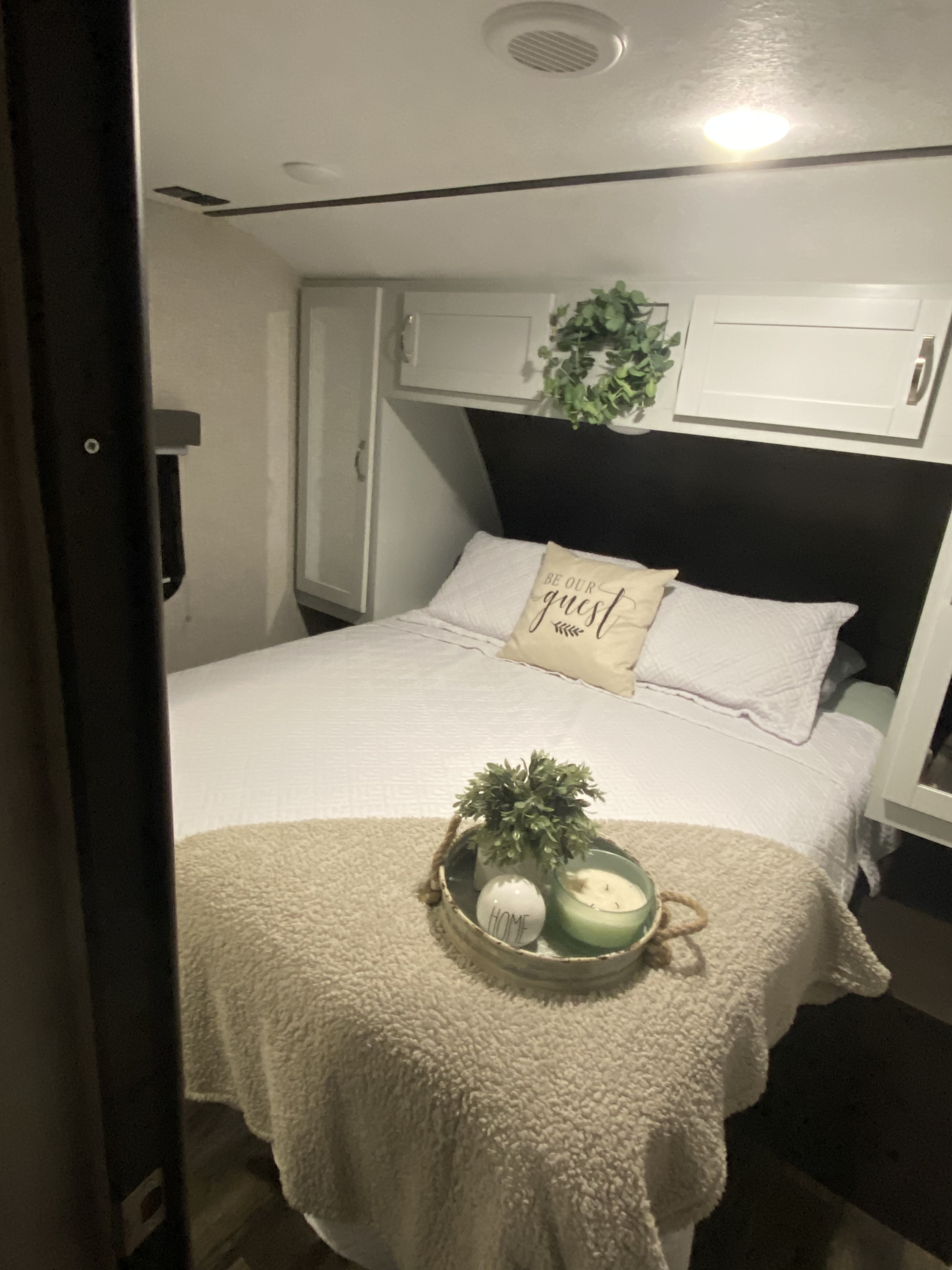 Cozy RV rental bedroom featuring white bedding, overhead storage, and a decorative tray with plants and candles.. Keystone RV Bullet Ultra Lite 2019