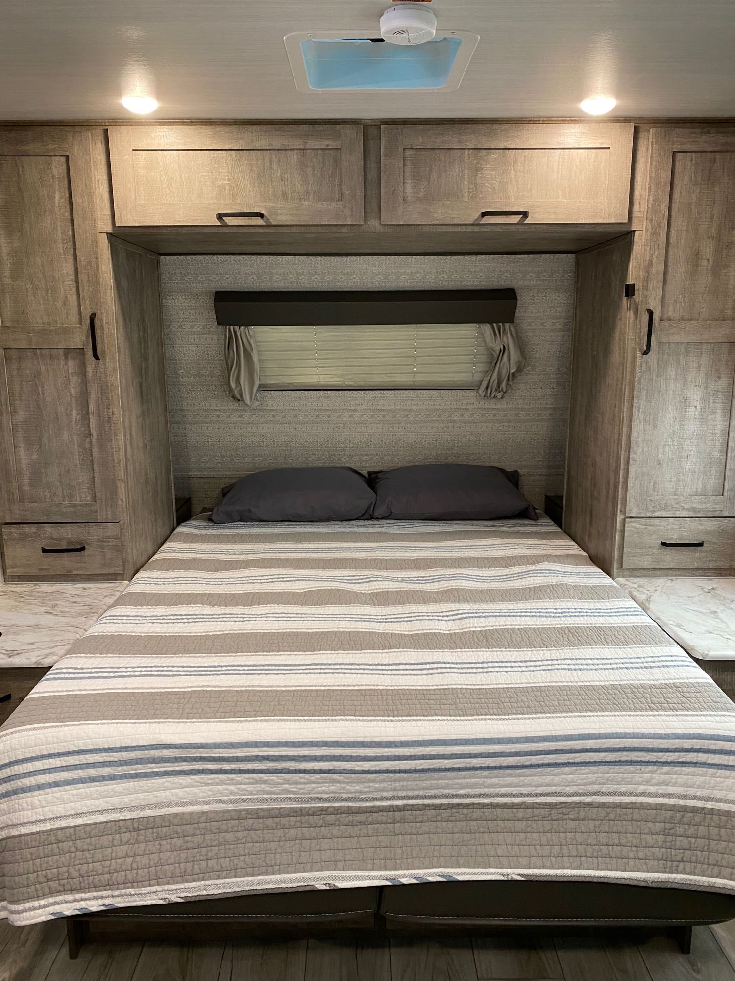RV rental's compact bedroom features a striped bed, grey pillows, and ample wood cabinets/storage.. Forest River Surveyor 2023