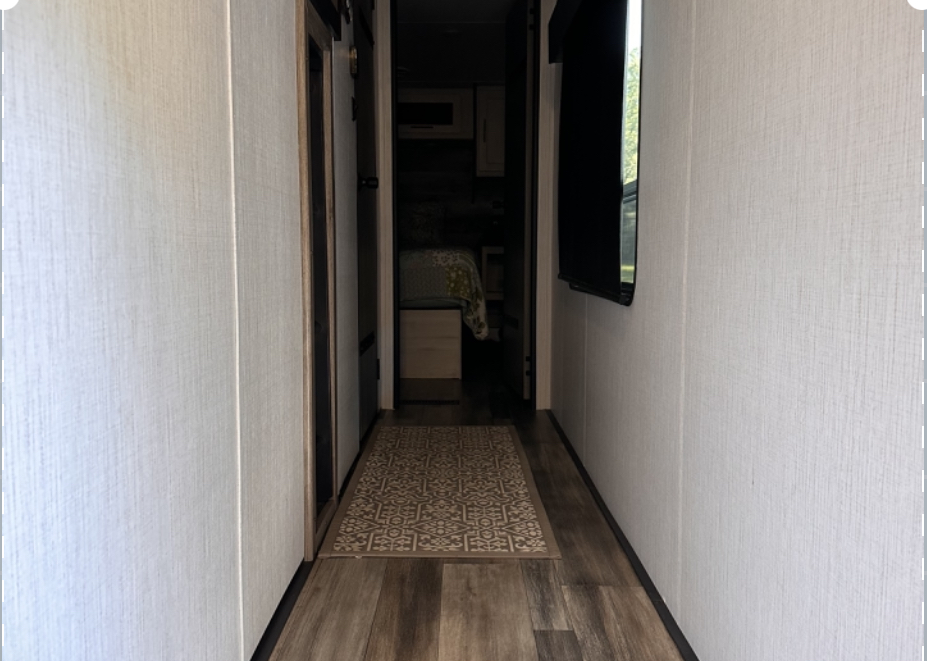 Step into this modern RV rental hallway, featuring wood-look flooring, light paneling walls, a mounted TV, and a bedroom entrance.. Heartland RVs Milestone 2022