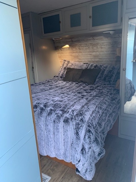 Cozy RV rental bedroom with a plush, grey-and-white bed, wood accent wall, and overhead storage for comfy travel.. Pilgrim International Inc Pilgrim 2007