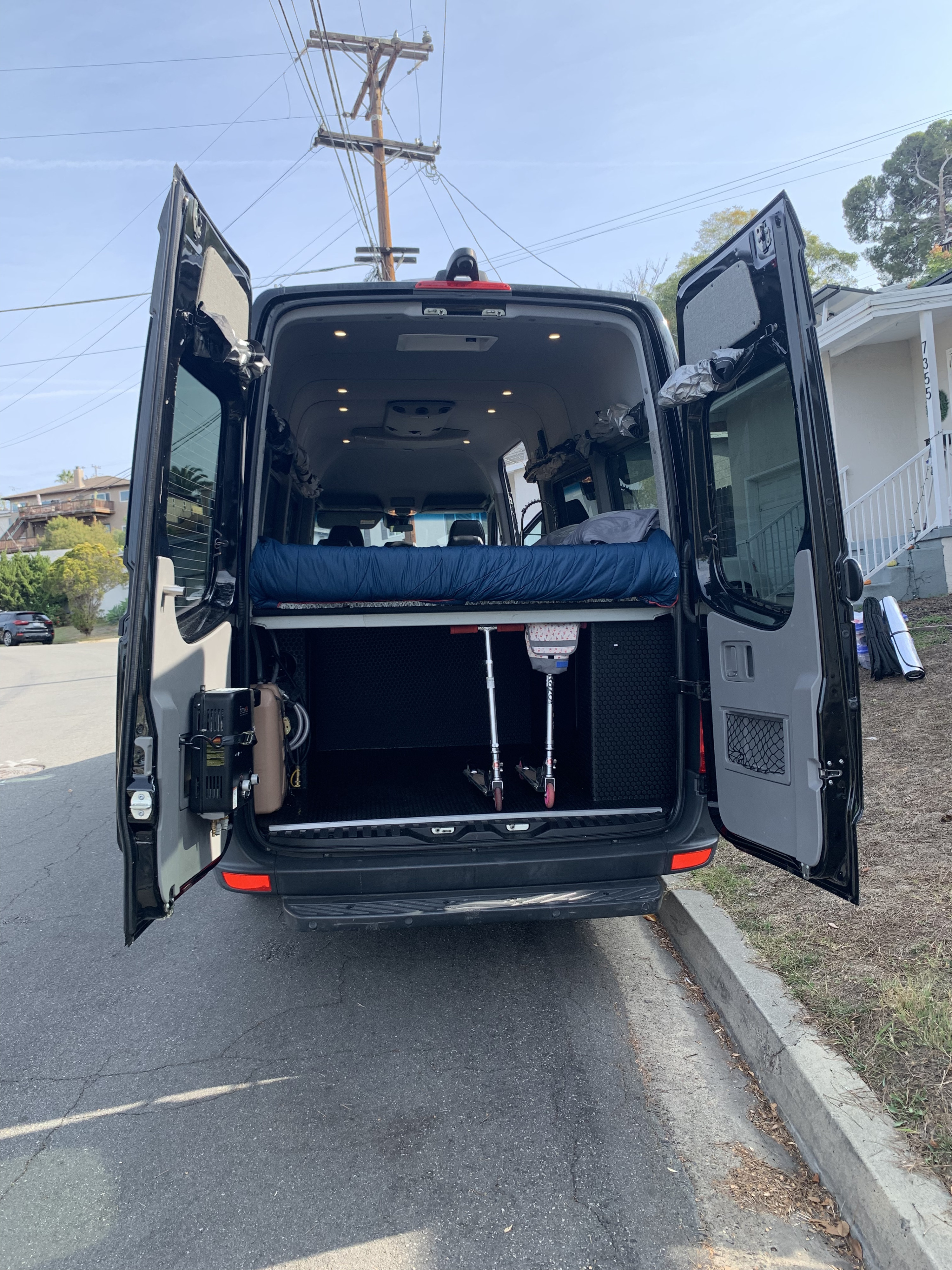 Interior of an RV rental camper van showing bed, storage, and scooters, ready for adventure.. Mercedes-Benz Sprinter 2018