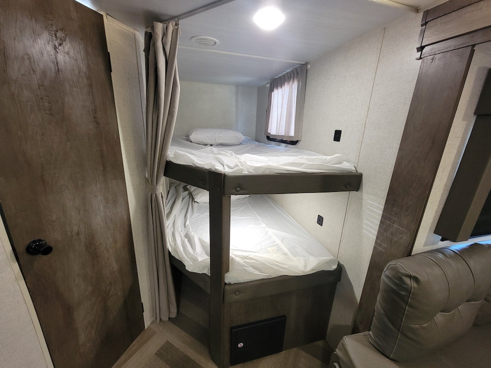Inside this RV rental: two compact bunk beds with white bedding, a privacy curtain, door, and small window. Ideal for travel.. Forest River Salem Cruise Lite 2020