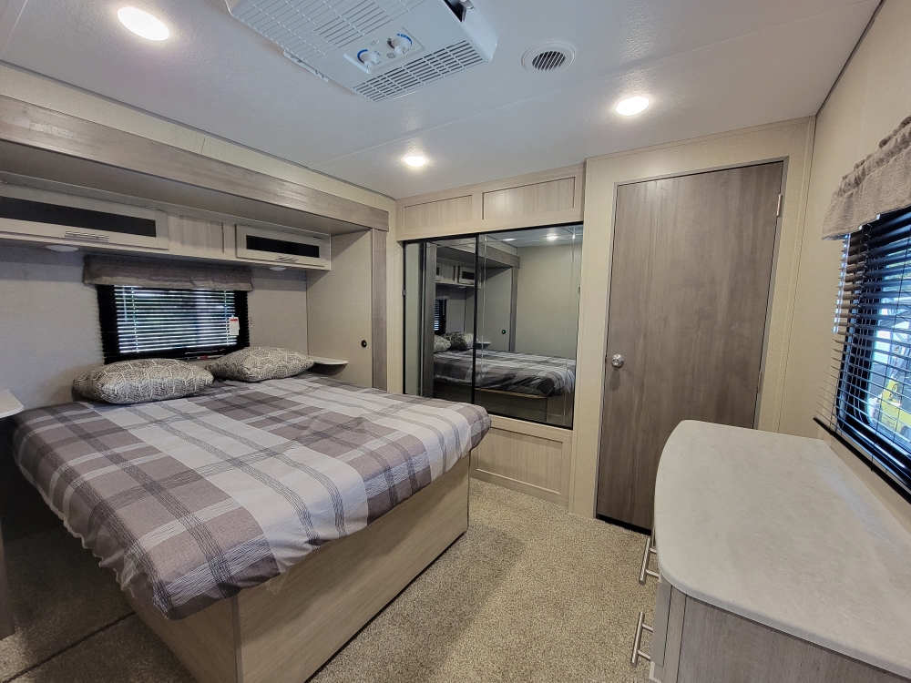 Step into comfort with this RV rental's inviting bedroom, featuring a queen bed, mirrored closet, and overhead storage.. Forest River Coachmen Catalina Legacy 2022