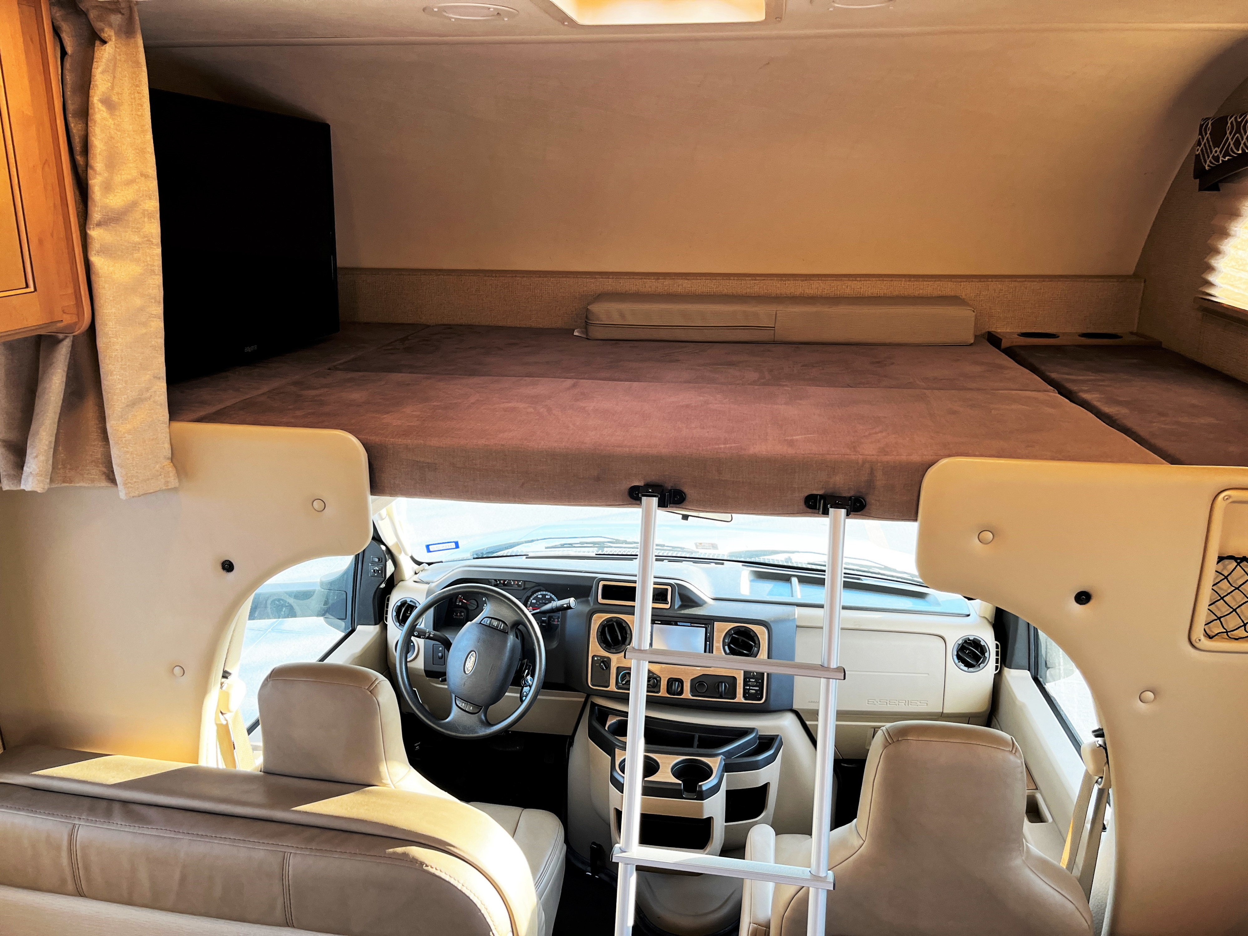 RV rental interior, showing a cozy over-cab sleeping area with ladder and front driving cabin.. Thor Chateau 2019