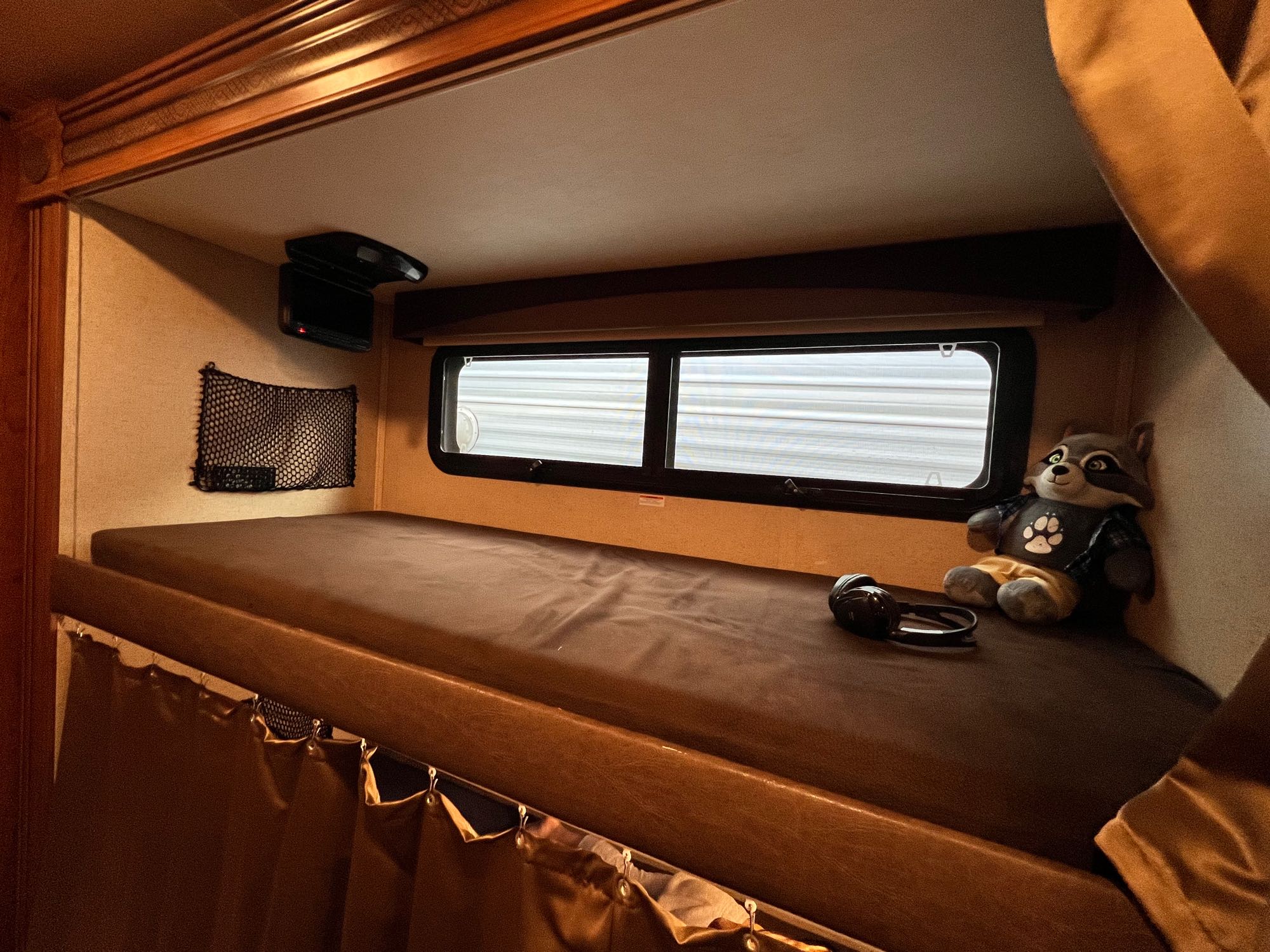 Cozy RV rental bunk bed interior: a comfortable sleep space with windows, screen, and a cute raccoon toy.. Jayco Greyhawk 2016