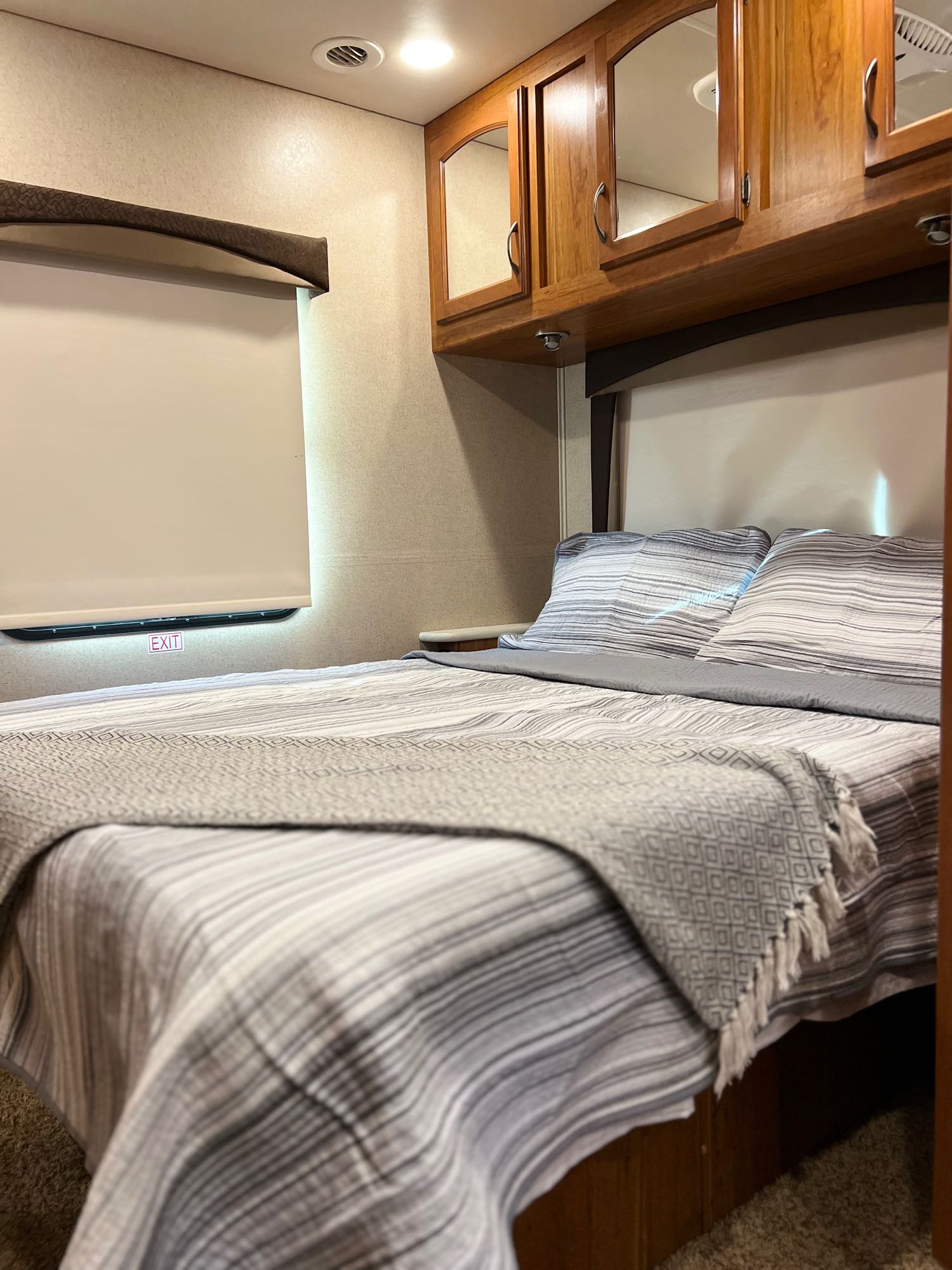 Inside an RV rental: a compact bedroom featuring a comfortable bed with striped linens, overhead storage, and an emergency exit.. Jayco Greyhawk 2016