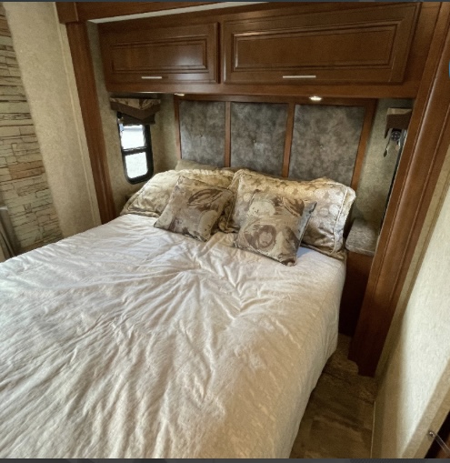 RV rental bedroom: Cozy space with a bed, decorative pillows, wooden cabinets, and a paneled headboard with lights.. Georgetown XL 2015
