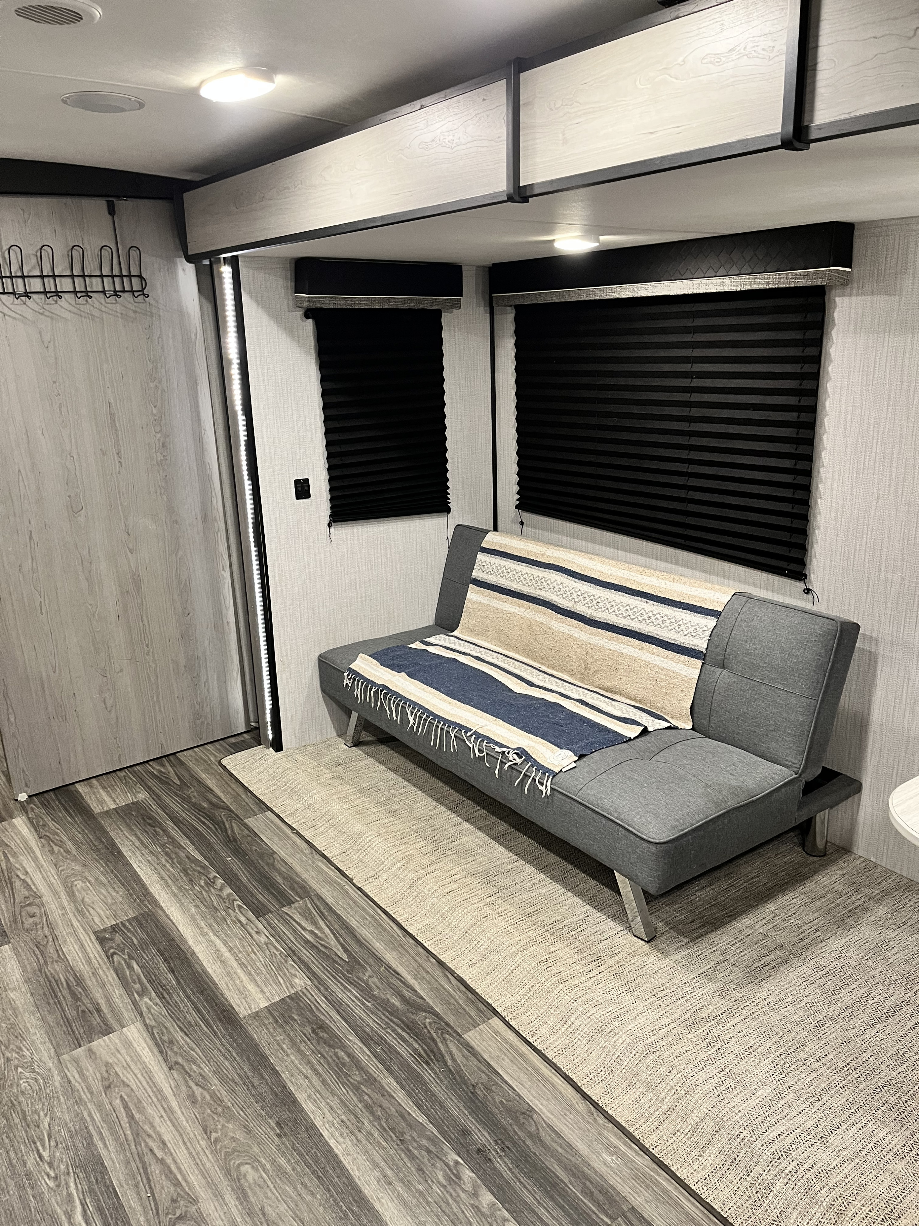 Bright and modern RV rental living space featuring a comfortable futon, black blinds, and sleek overhead storage.. Heartland RVs Mallard 2021