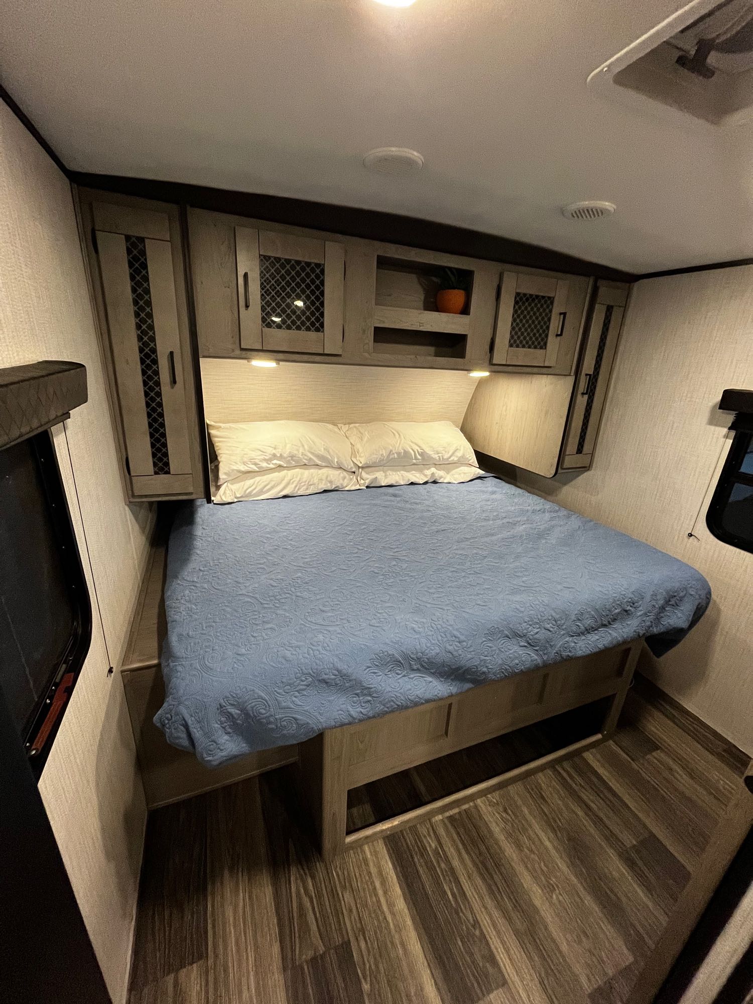 Spacious RV rental bedroom with a comfy queen bed, built-in storage, under-bed space, and wood floors.. Heartland RVs Mallard 2021