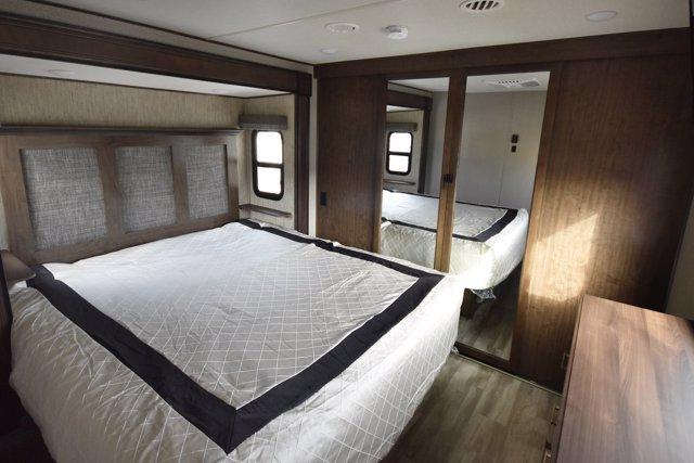 Comfortable RV rental bedroom with a large bed, textured headboard, mirrored closet, and wood furnishings.. Grand Design Solitude 2020