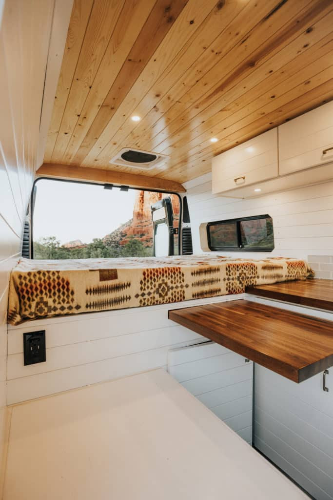 Cozy RV rental interior: wooden ceiling, white walls, bed with patterned cover overlooking a scenic view, and wood counters.. Dodge Sprinter 2018