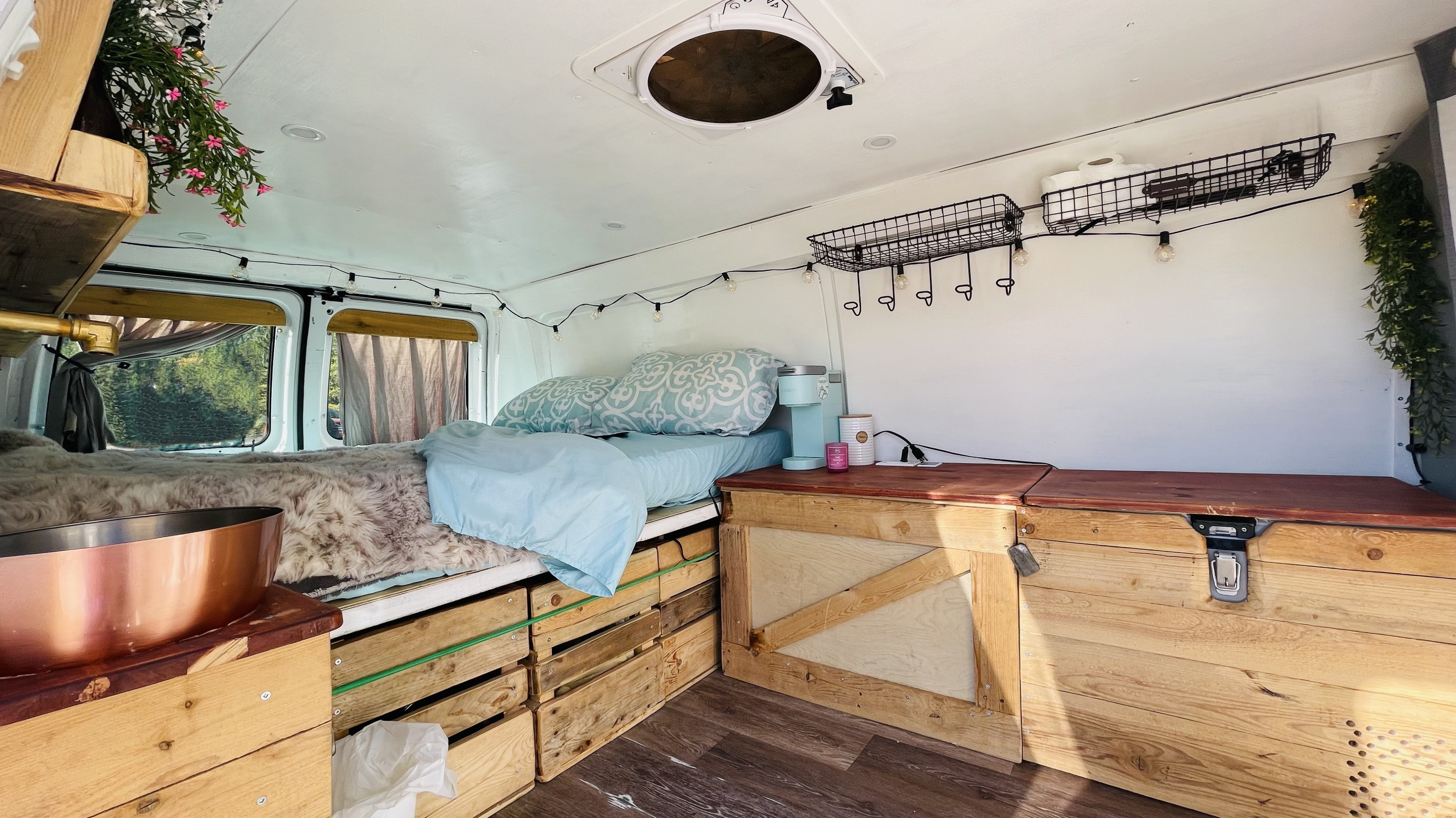 Cozy RV rental interior: bed, wooden storage, coffee station, & string lights create a comfortable mobile living space.. Ford Econoline 2012