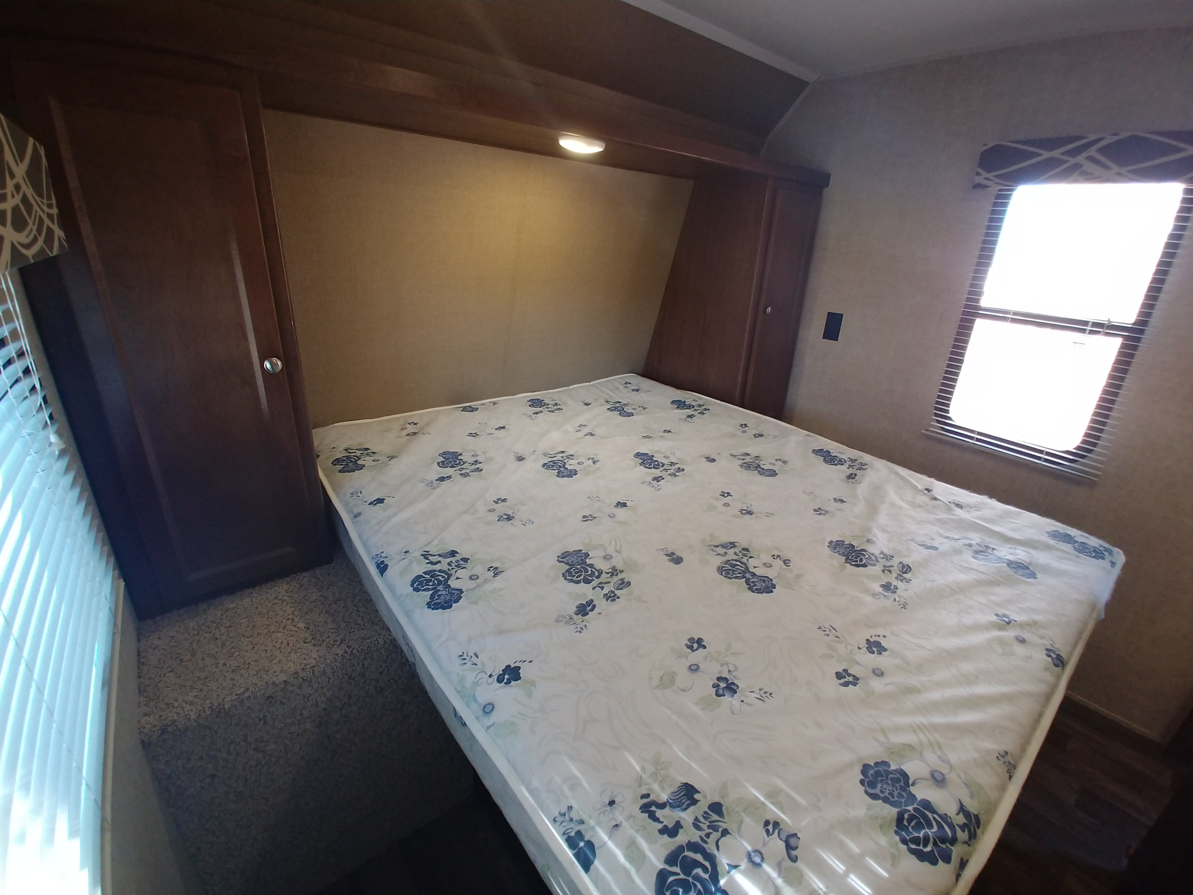 Cozy RV rental bedroom with a white mattress featuring blue flowers, built-in wooden cabinets, and a window.. Keystone RV Hideout LHS 2017