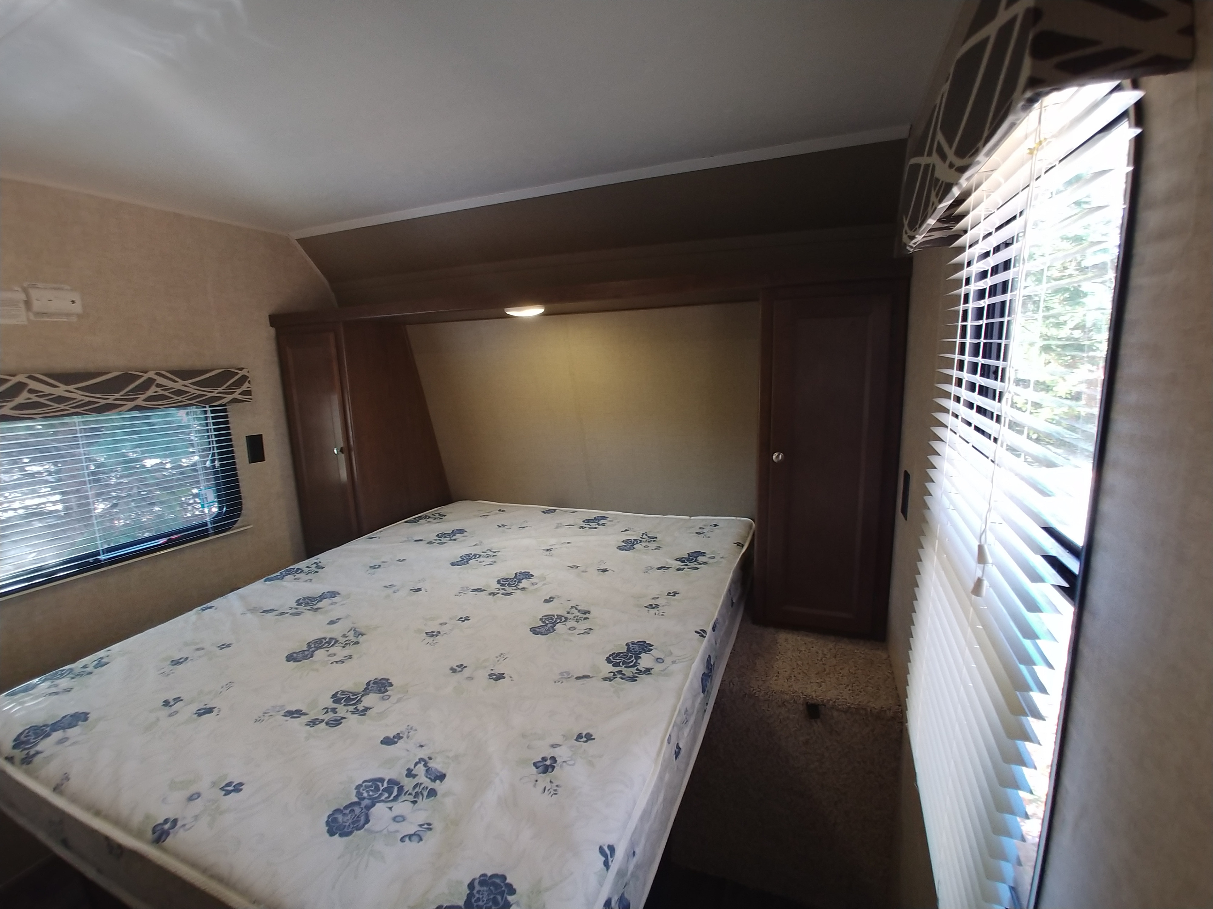 RV rental bedroom interior: Features a bed with floral mattress, windows, and built-in storage cabinets.. Keystone RV Hideout LHS 2017