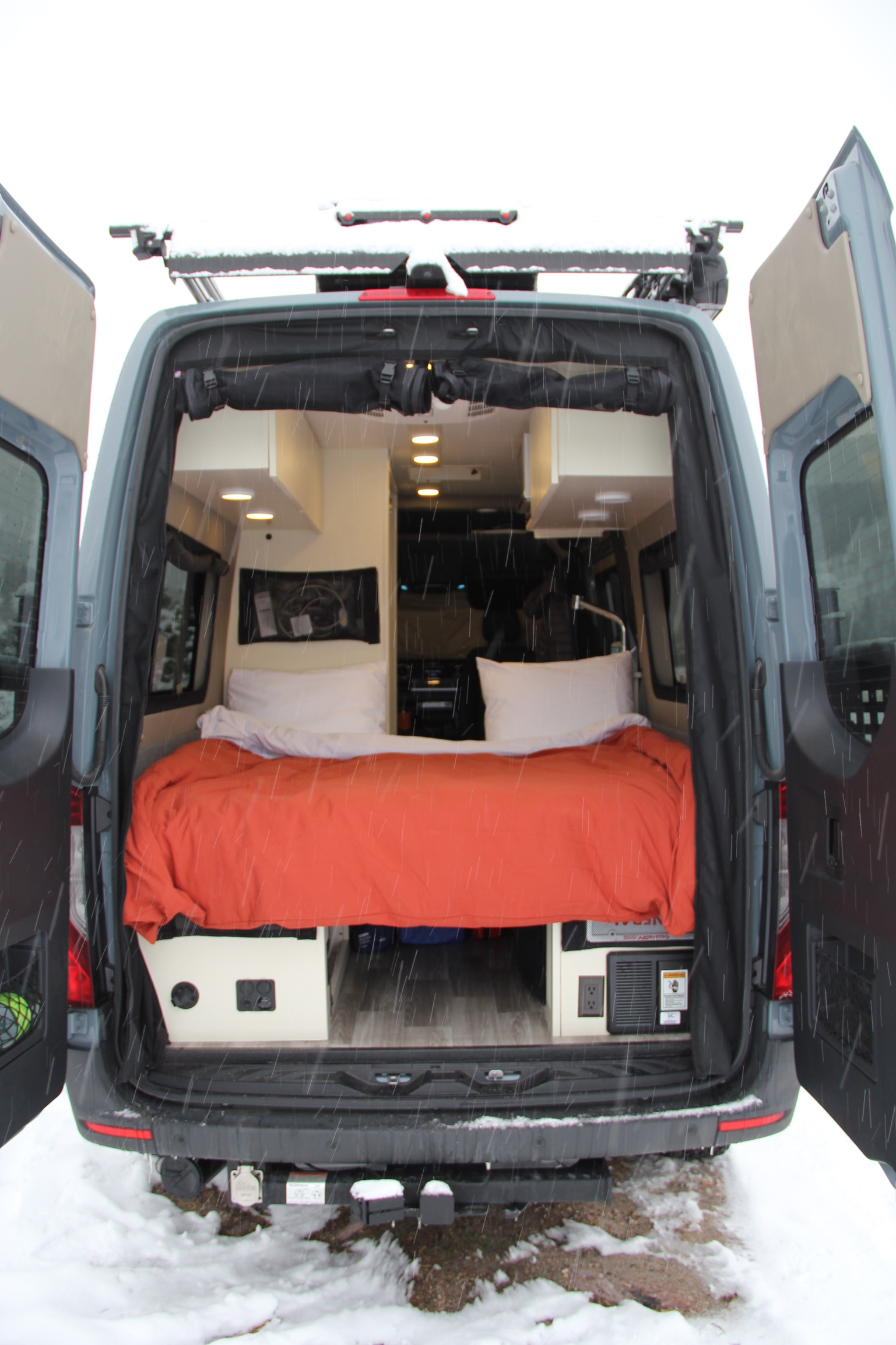 Explore in comfort with this RV rental camper van. Rear doors open show a cozy bed, custom interior, ready for winter travel.. Mercedes Sprinter Van 2022