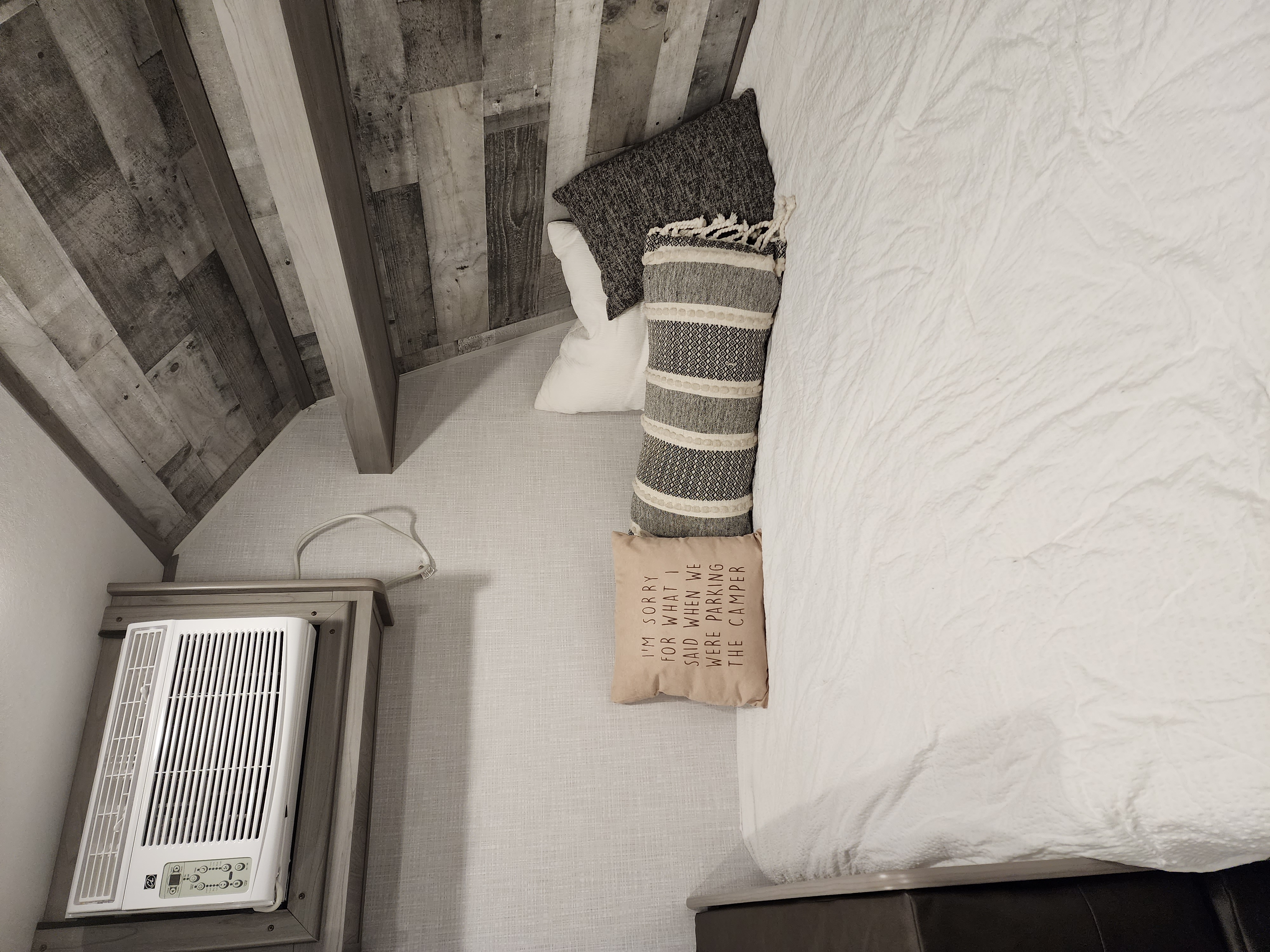 Cozy RV rental bedroom with rustic wood ceiling, comfy bed, decorative pillows, and an AC unit.. Coleman Lantern 17b 2023