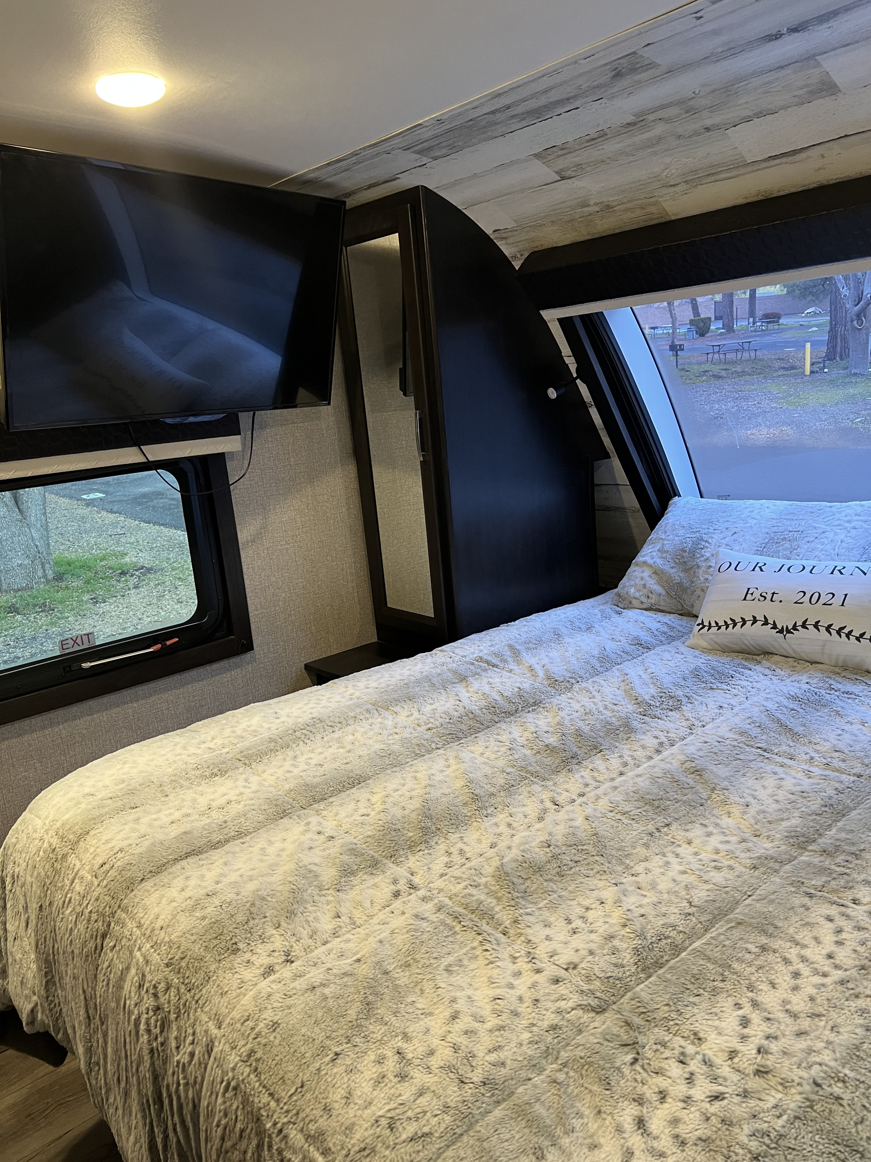 Cozy RV rental bedroom featuring a soft bed, TV, and window view of a peaceful campground. Ideal for your journey.. Jayco White Hawk 2021