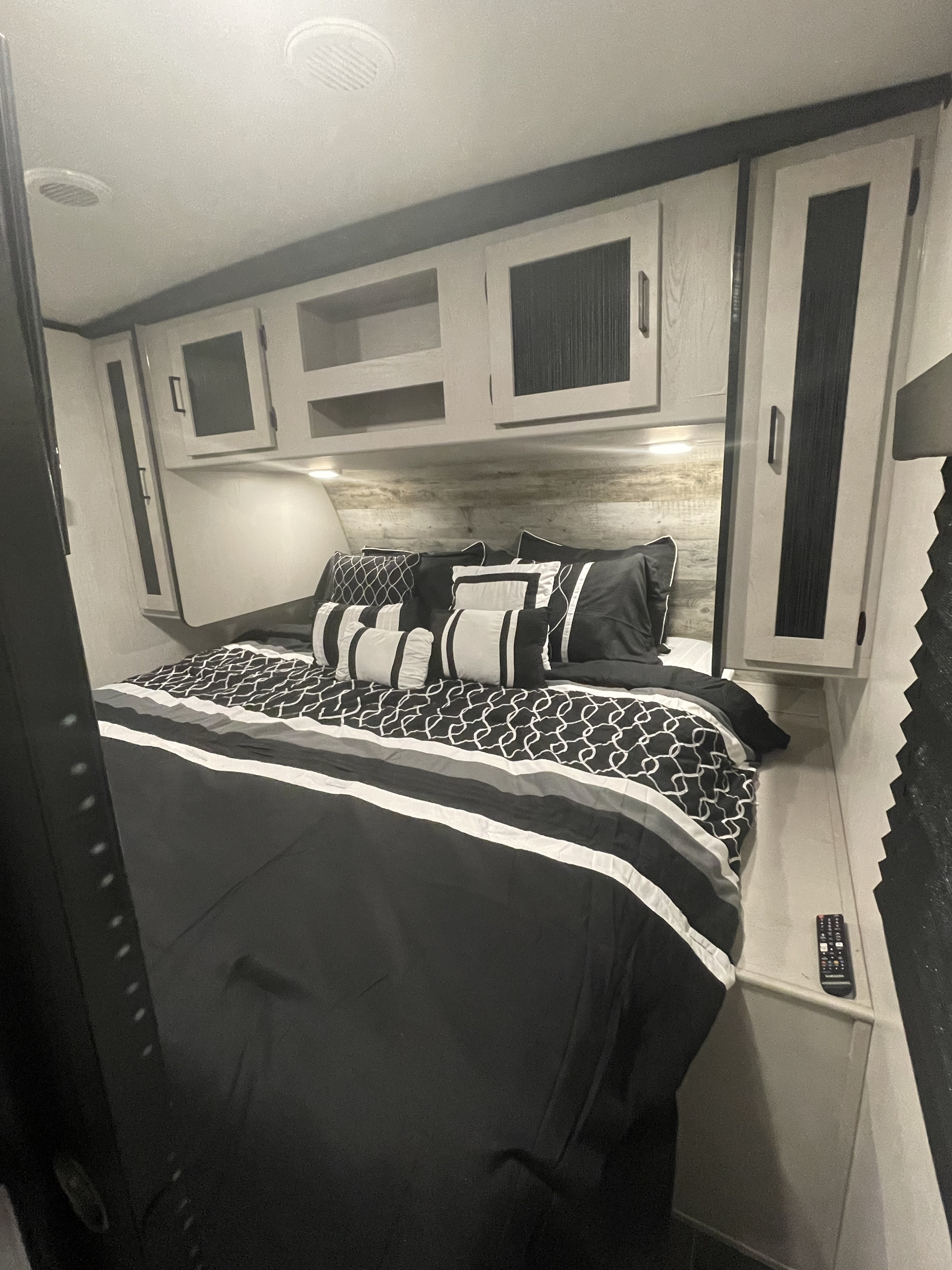 Modern RV rental bedroom featuring crisp black and white bedding, ample overhead storage cabinets, and a comfortable sleeping area.. Heartland RVs Mallard 2022