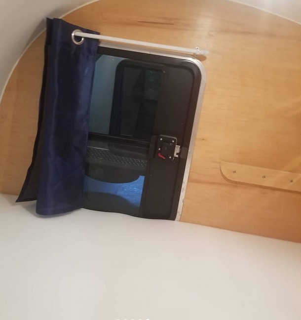 Cozy RV rental interior: bed, wood walls, blue curtained window, and a small wooden shelf.. The Teardrop Trailer Inc Silver Bullet upgraded 2022