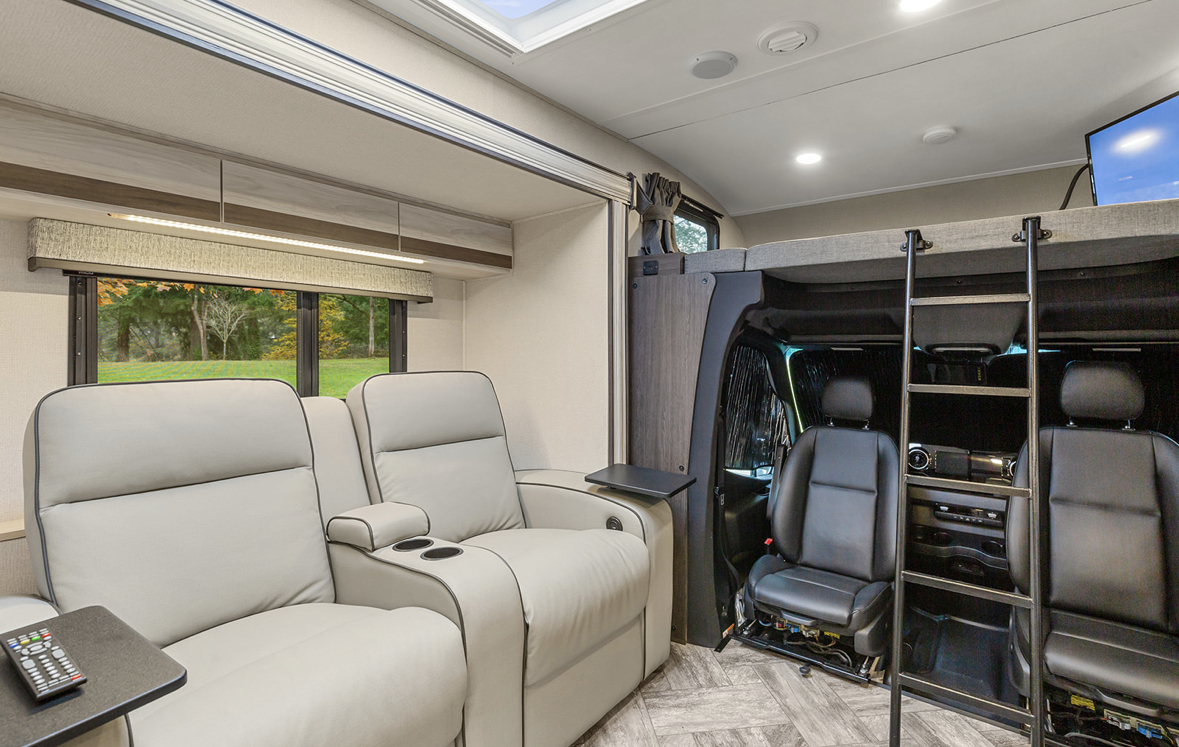 Spacious rv rental interior featuring light recliners by a window, and a bunk bed over the vehicle's cockpit area.. Forester MBS 2022