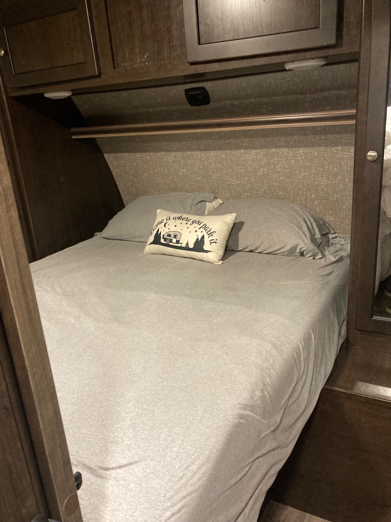 Cozy RV rental bedroom featuring a made bed with grey linens and a decorative "Home is where you park it" pillow.. Heartland RVs Sundance XLT 2017