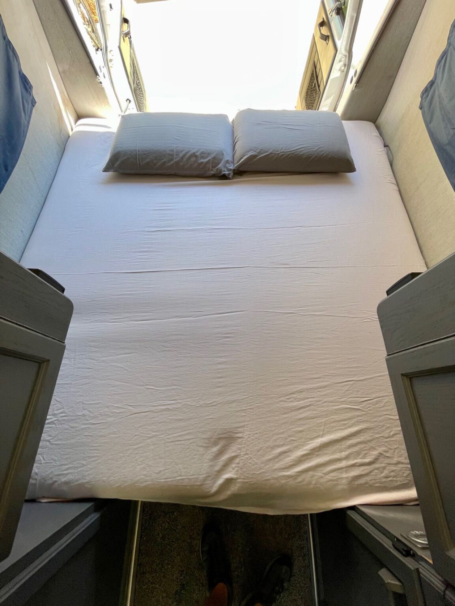 Cozy RV rental sleeping area, ready for adventure. A compact bed with pillows inside a camper van.. Roadtrek 210 - Popular 1996