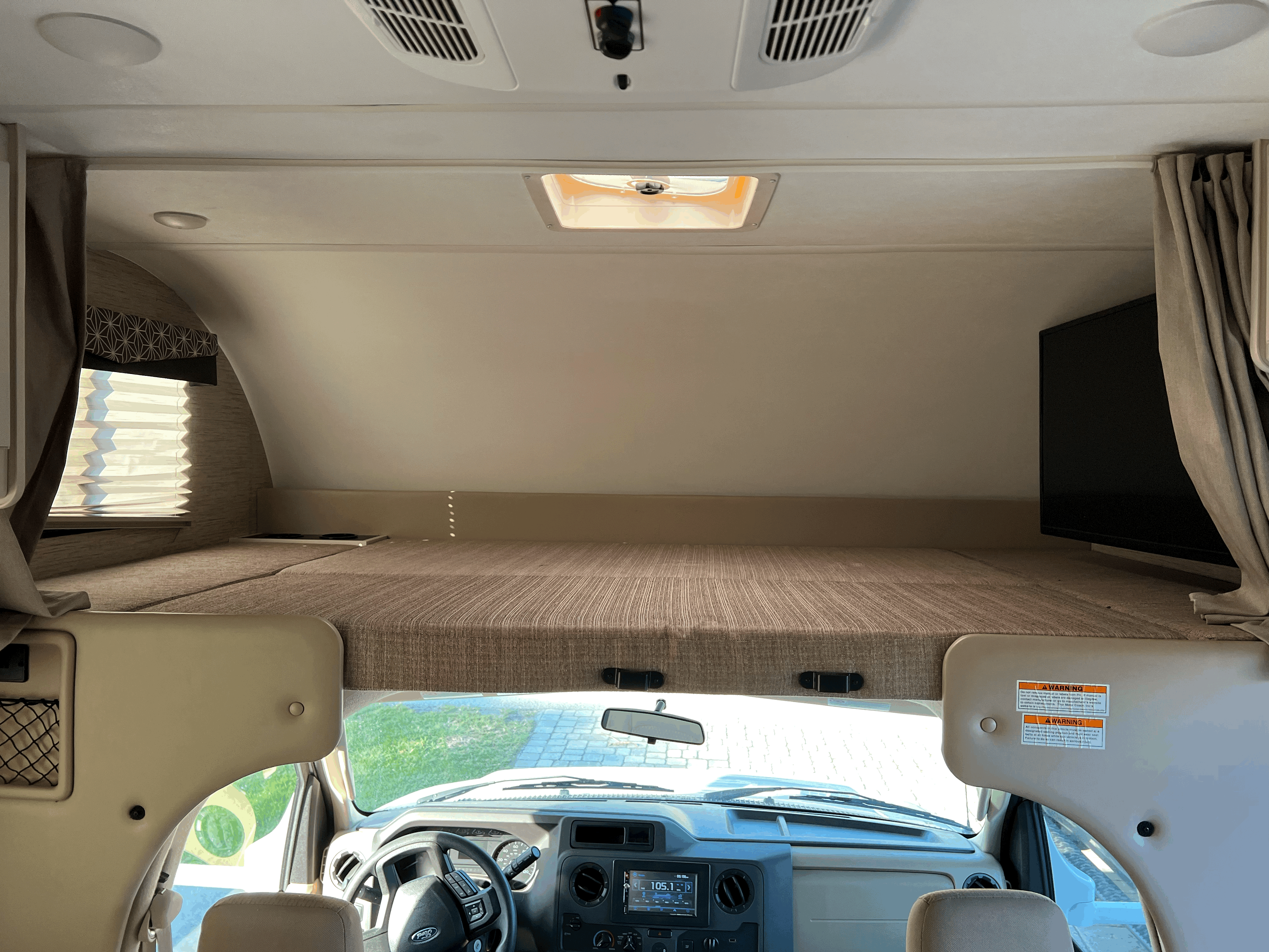 Inside an RV rental, featuring the spacious overhead bunk, driver's cockpit with Ford dashboard, window, and TV.. Thor Freedom Elite 2022