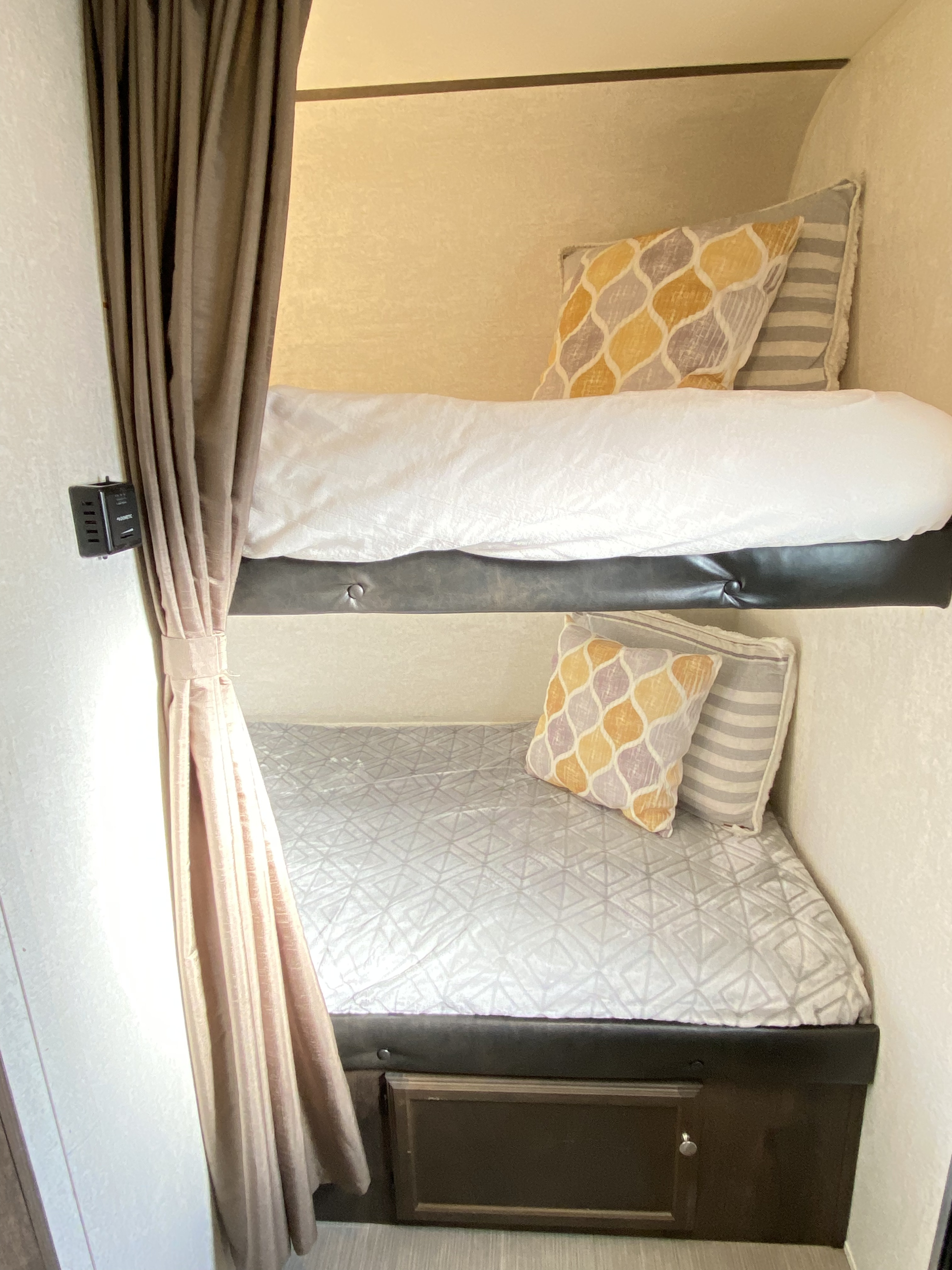 Cozy RV rental bunk beds with colorful pillows, white bedding, and a privacy curtain. Features compact sleeping & lower storage.. Starcraft Launch 2018