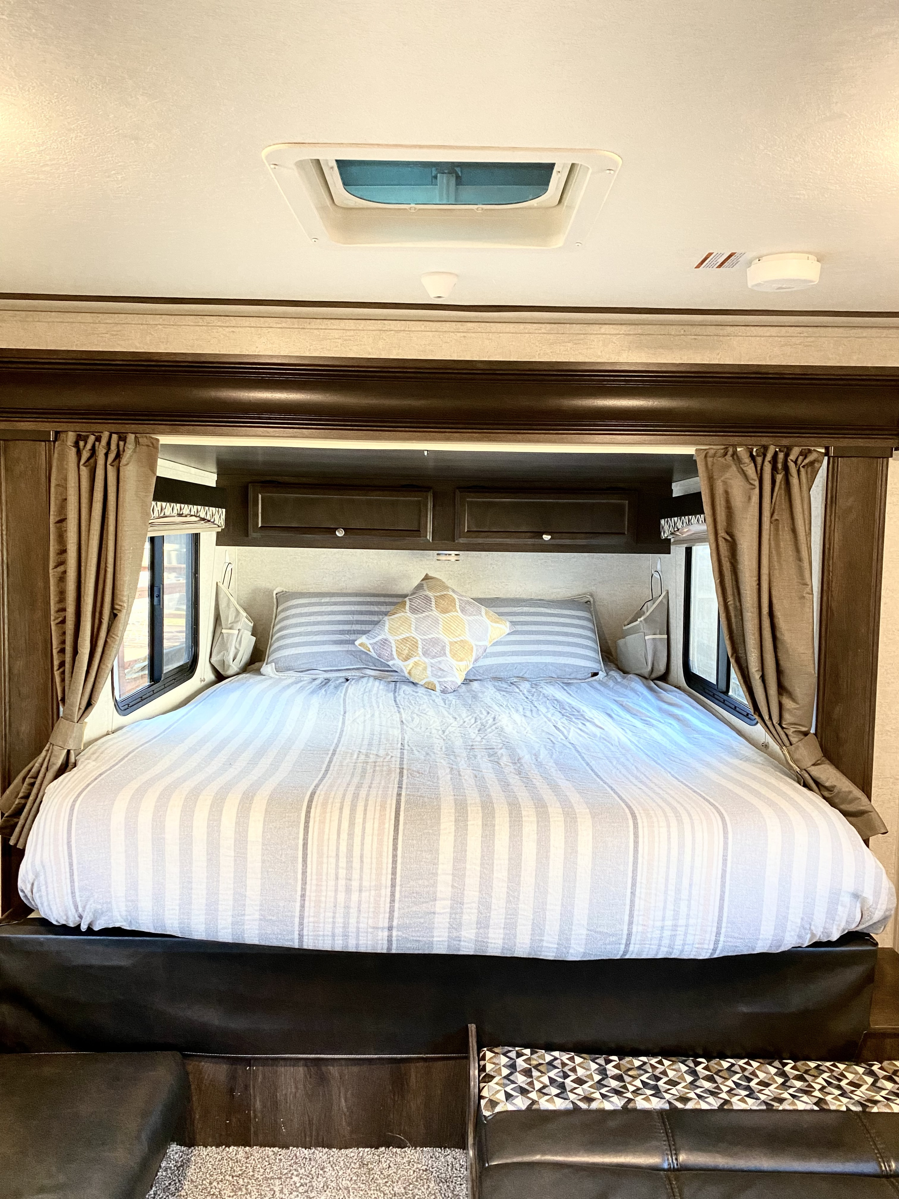 This RV rental bedroom features a comfy striped bed, side windows with curtains, and ceiling vent, perfect for rest.. Starcraft Launch 2018