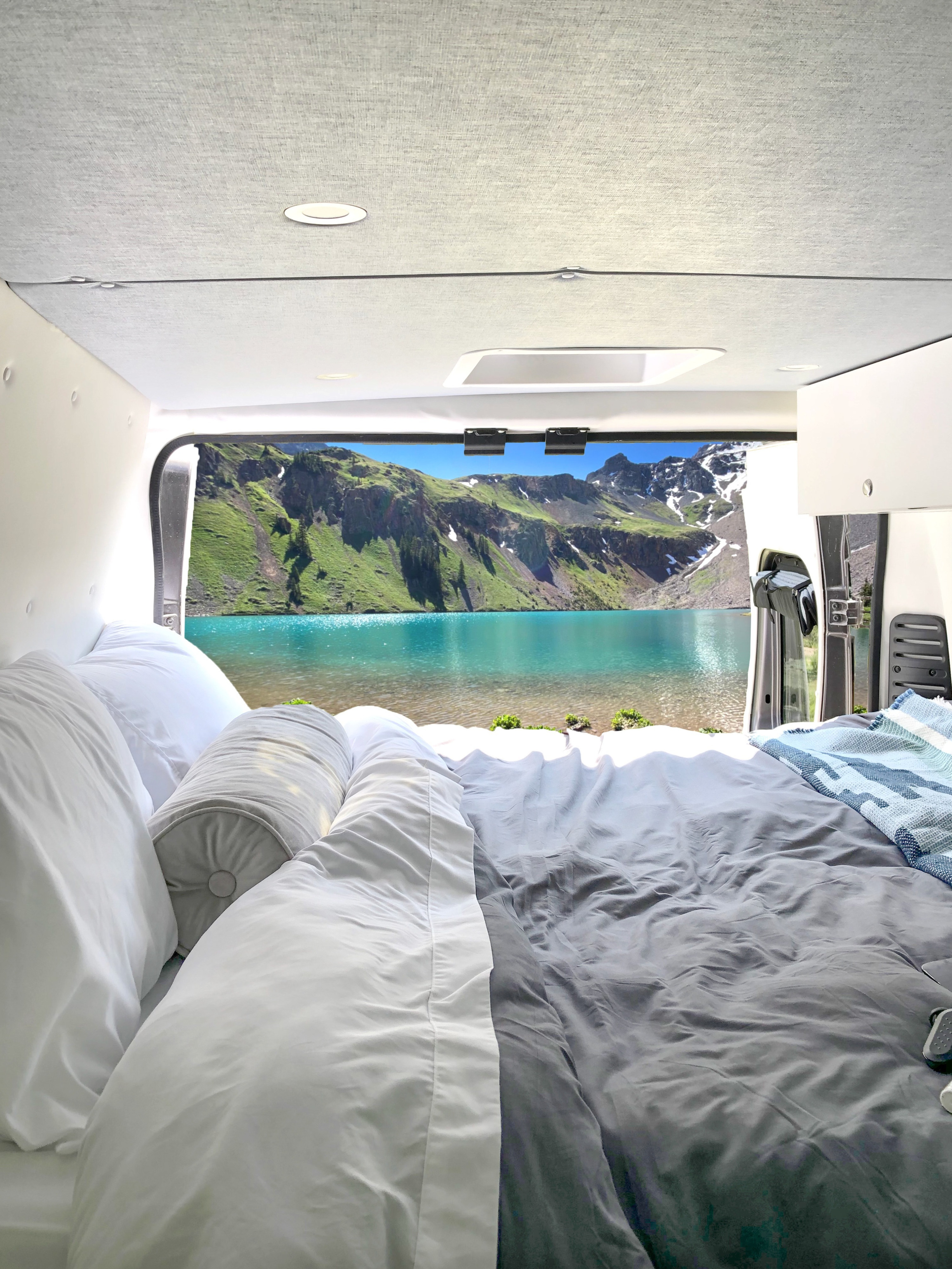 RV rental camper van with open back doors showcasing a stunning turquoise lake and mountain view from a cozy bed.. Dodge 2500 Promaster 2021