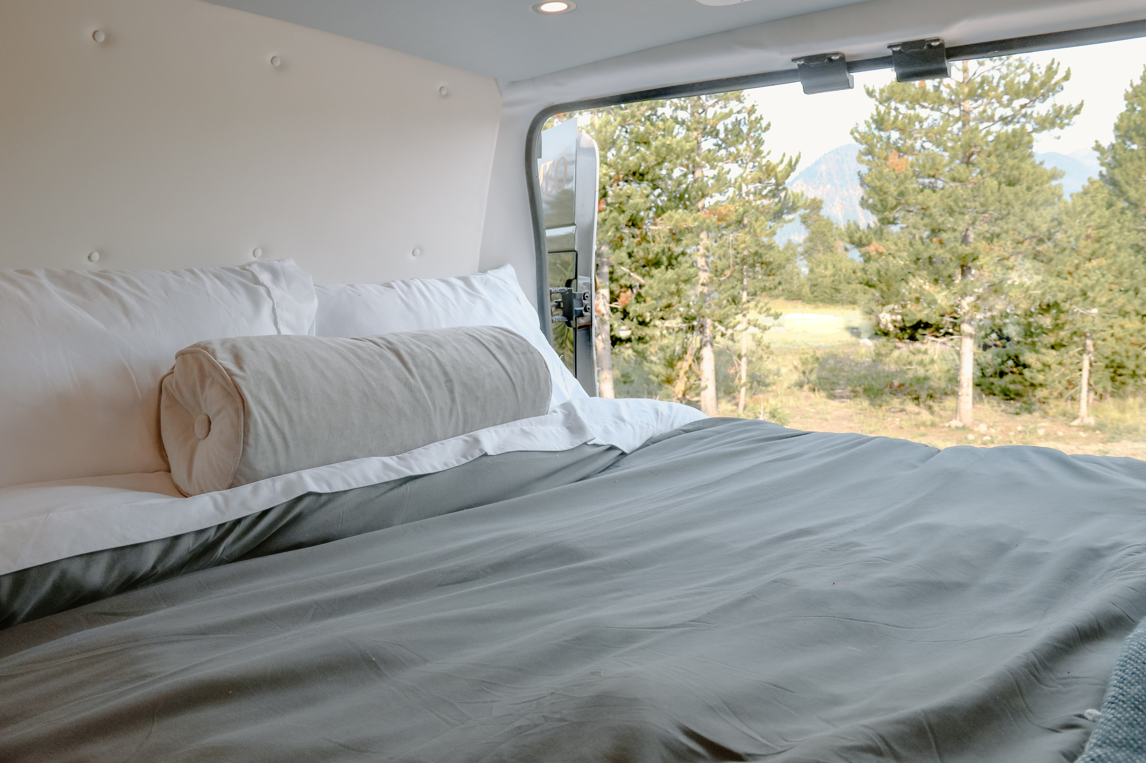 RV rental: inviting bed with white linens and grey duvet, offering stunning views of pine trees and mountains.. Dodge Other 2021
