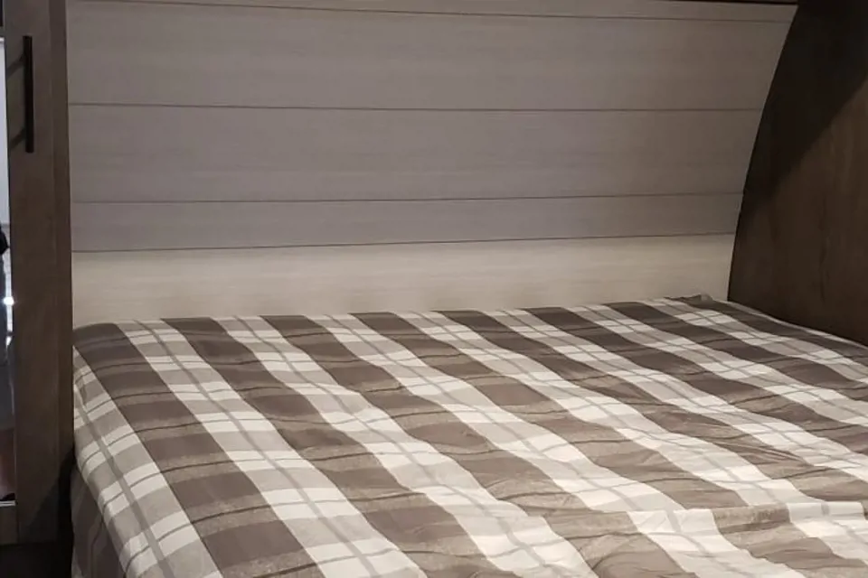 Inside this RV rental: a comfortable bedroom featuring a plaid bedspread and light wood-paneled headboard.. Forest River Salem 2022