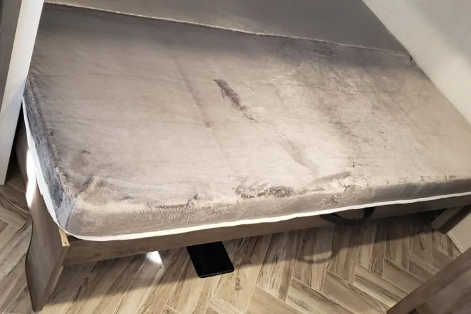 An unmade bed with a rumpled gray blanket in this RV rental. A black phone is on the patterned floor below.. Forest River Salem 2022