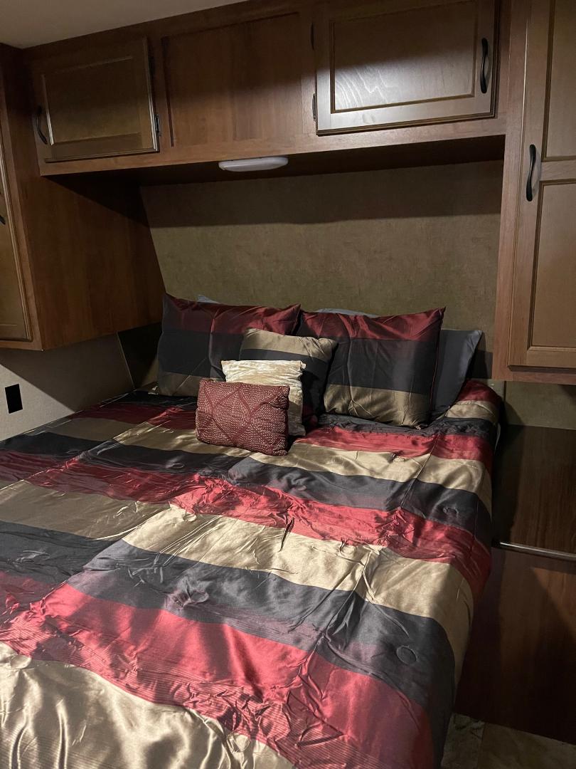Cozy RV rental bedroom featuring a striped comforter, multiple pillows, and practical overhead storage cabinets.. Jayco Jay Flight 2015