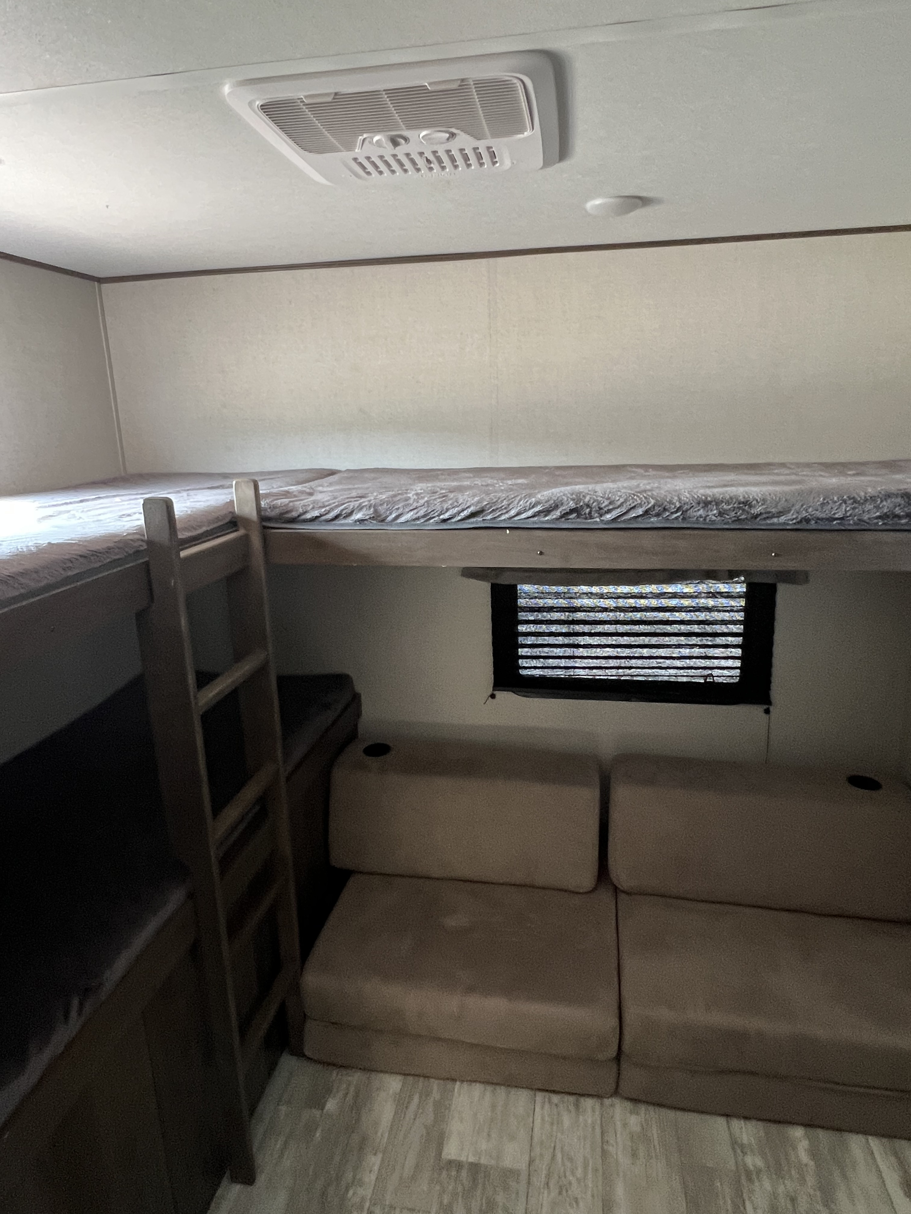 An RV rental interior showing a bunk bed setup with ladder, a convertible sofa, and ceiling AC. Comfortable family space.. Avenger Avenger Trailer 2021