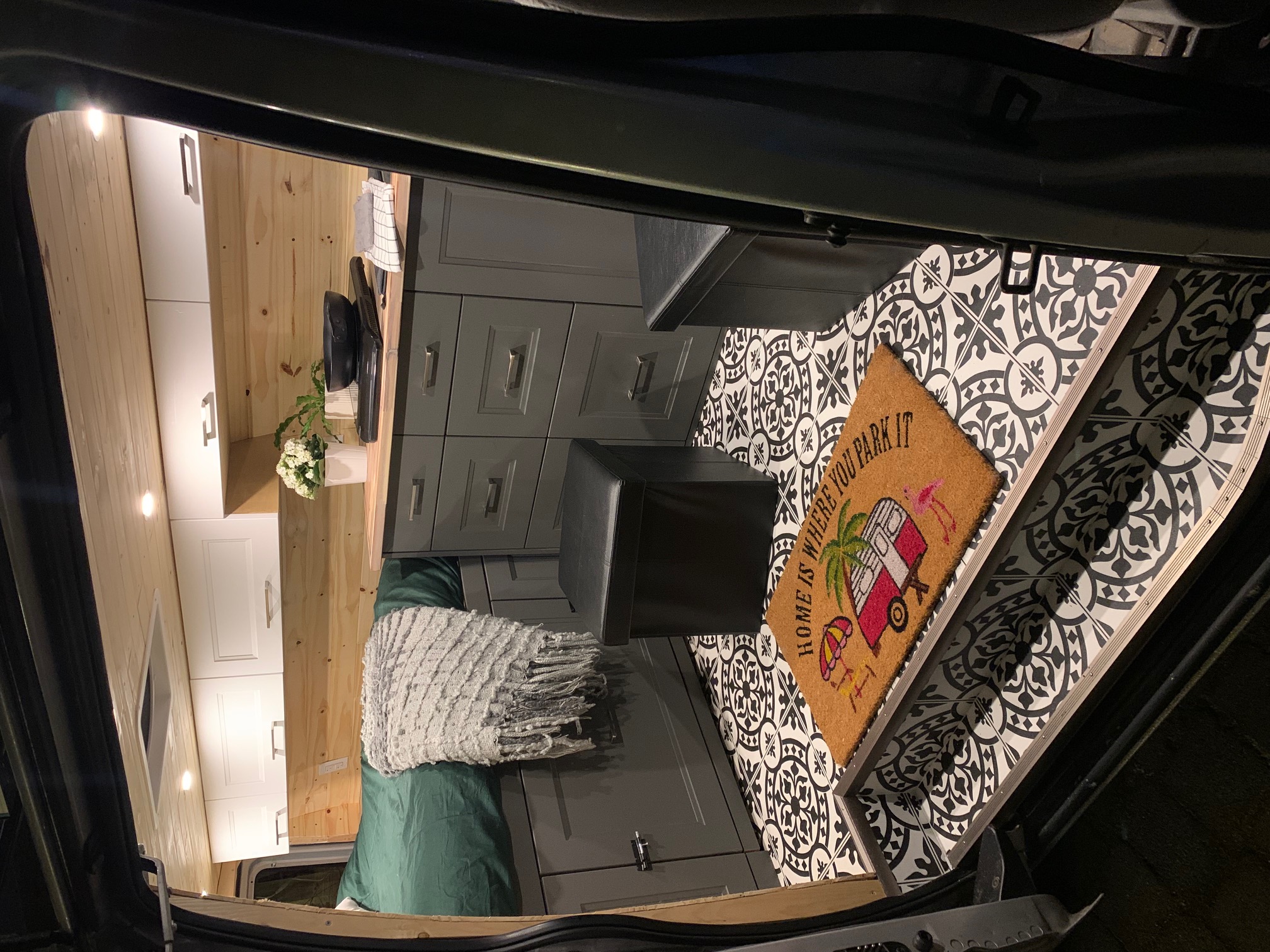 Cozy RV rental interior with wood walls, white & gray cabinets, patterned floor, and a "Home is where you park it" mat.. Ford Econoline 2009