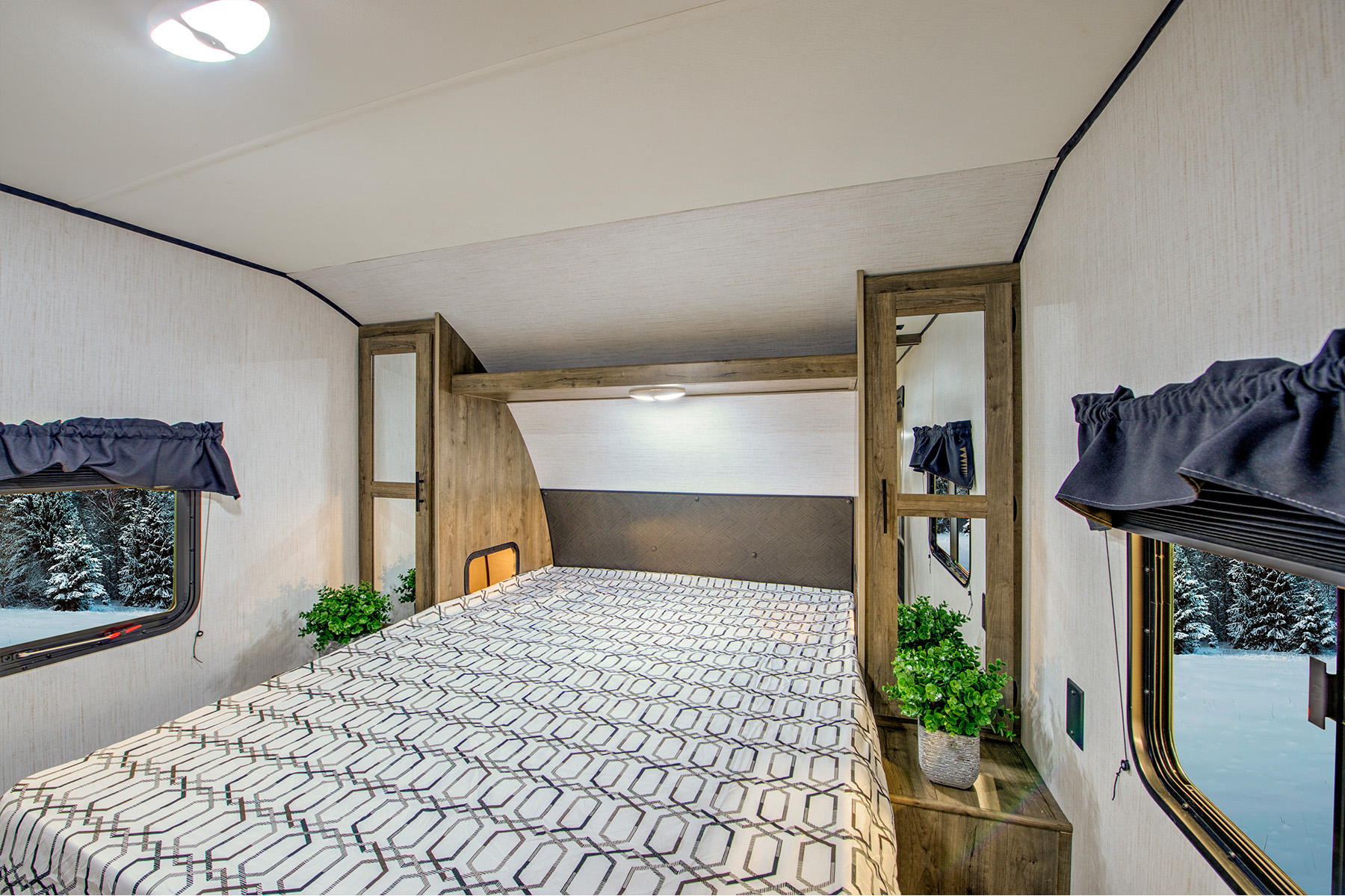 Cozy RV rental bedroom with a geometric patterned bed, wood accents, and winter forest views from the windows. Perfect for travel.. Heartland Pioneer 2022
