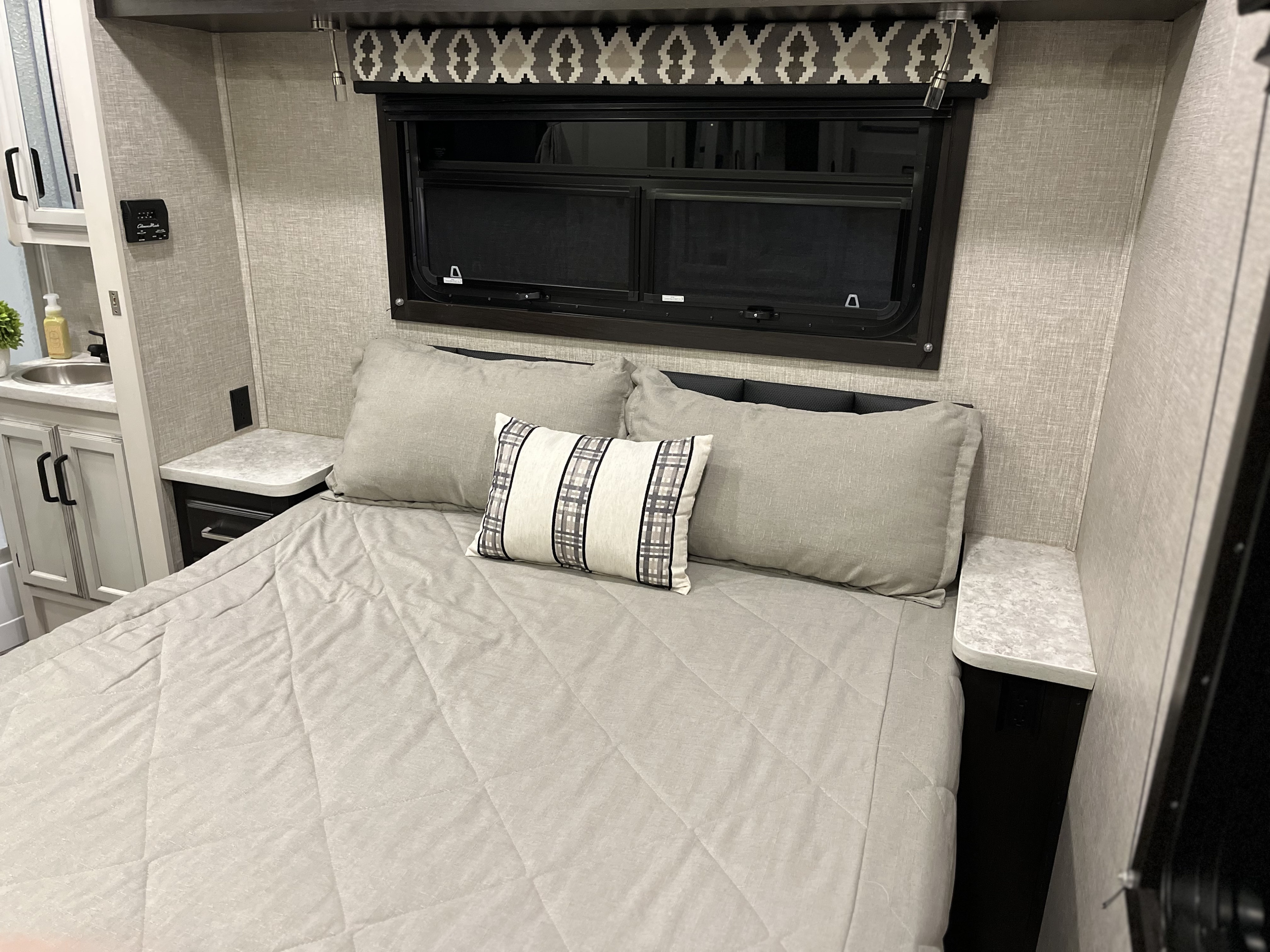 RV rental: Light gray quilted bed and decorative pillow in a modern bedroom with window, nightstands, and compact sink.. Jayco Redhawk 2022