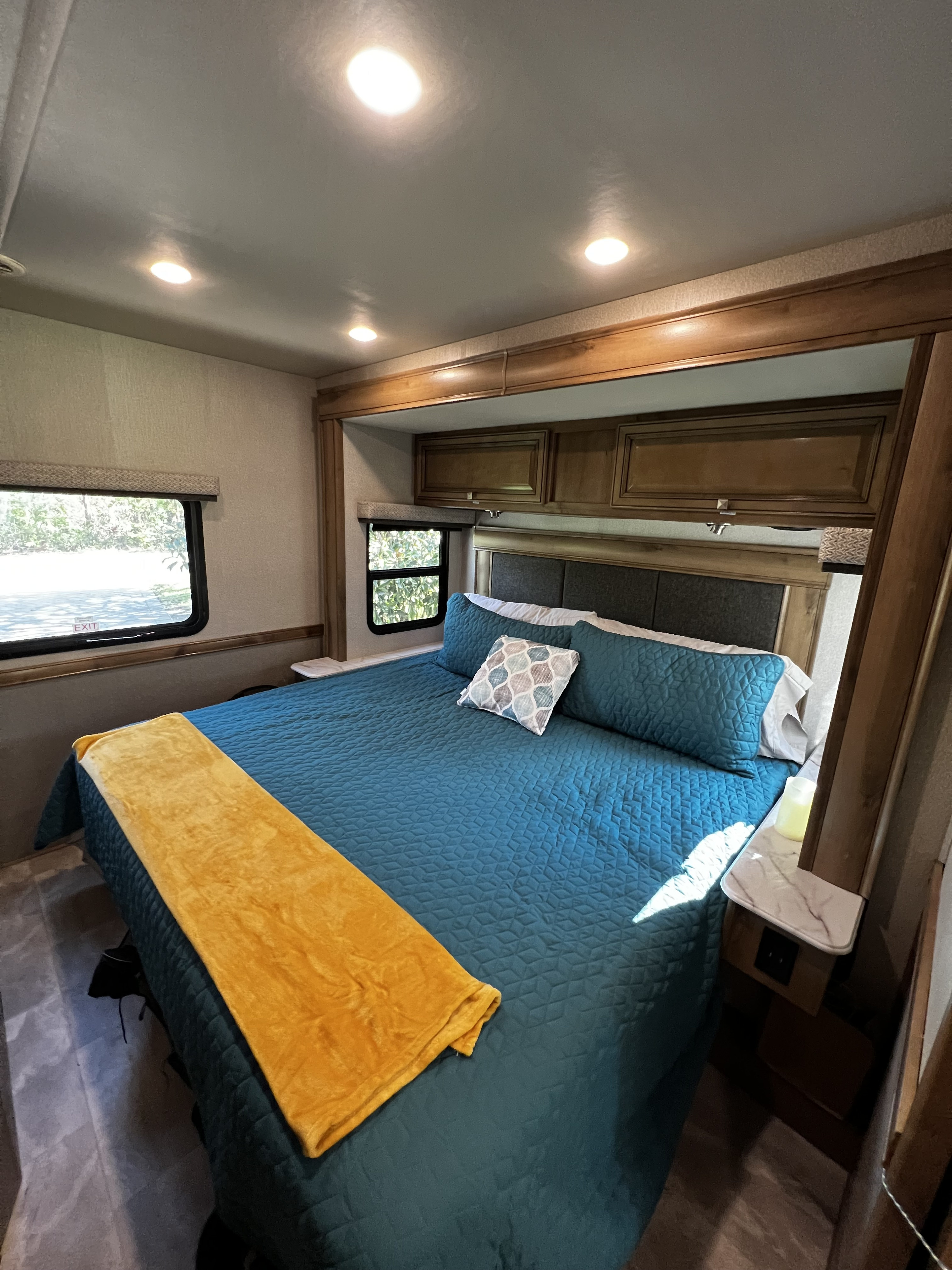 Cozy RV rental bedroom with a large bed, teal bedding, yellow throw, built-in cabinets, and scenic windows.. Holiday Rambler Admiral 2021