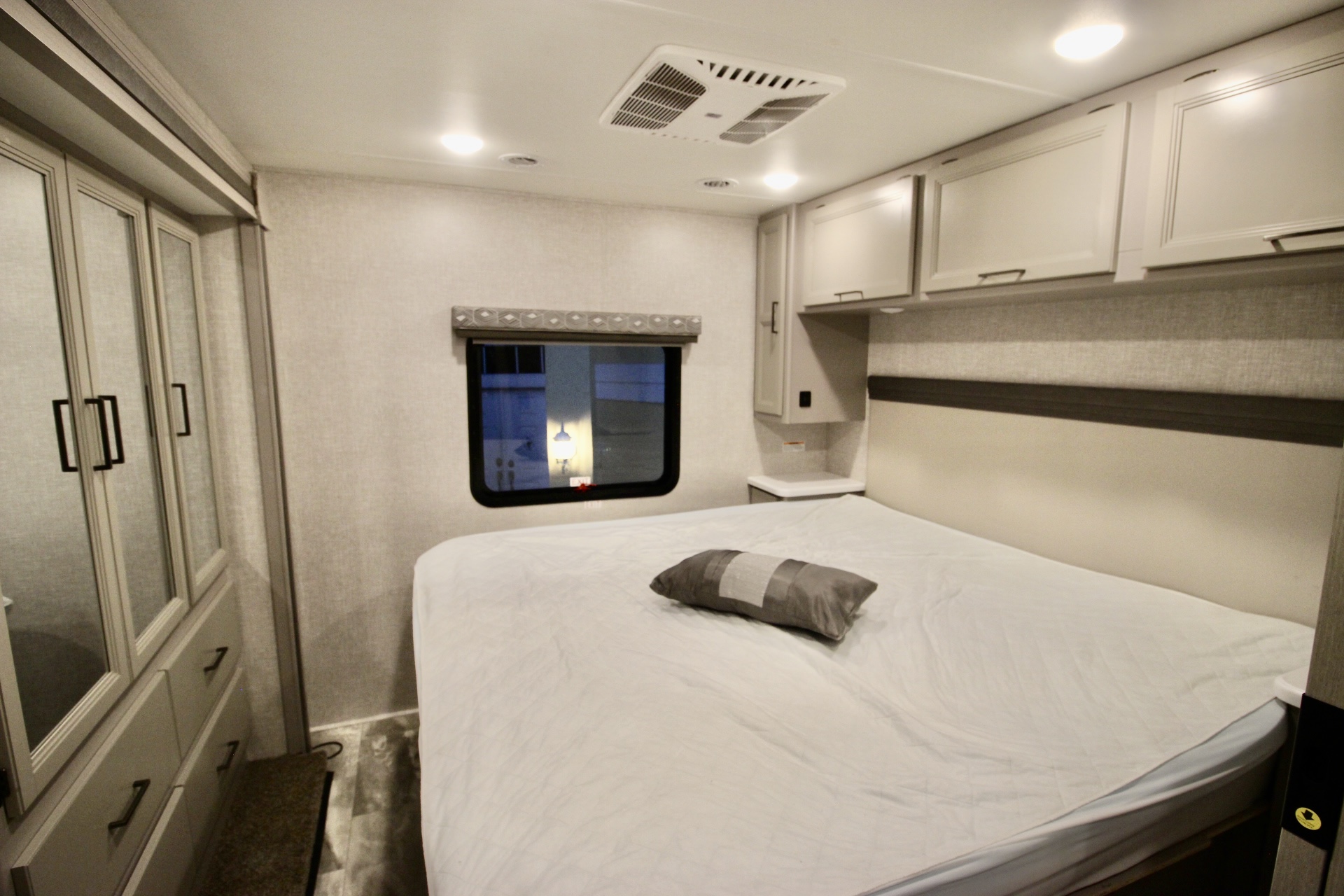 RV rental bedroom: large bed, grey pillow, window, plus ample storage via overhead cabinets & wardrobe.. Thor Motor Coach Windsport 2023