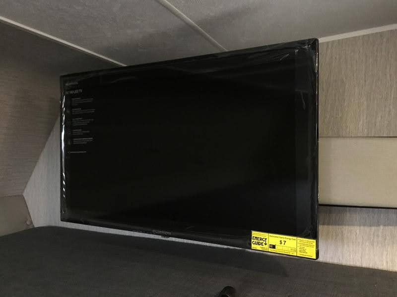 A new, plastic-wrapped flat-screen TV is mounted in an RV rental, ready for in-cabin entertainment.. Forest River Coachmen Freelander Premier 2022