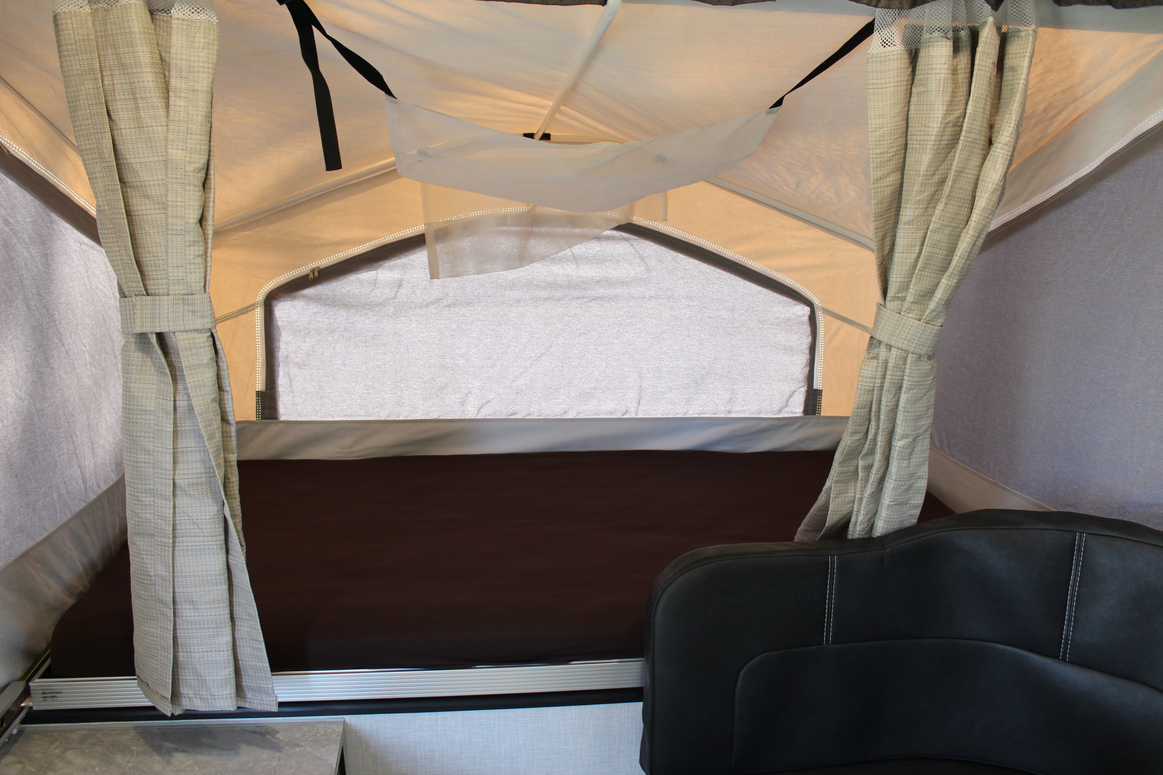 Interior of an RV rental pop-up camper showing tied-back curtains, a dark bed area, and part of a black seat.. Forest River Rockwood ESP 2021
