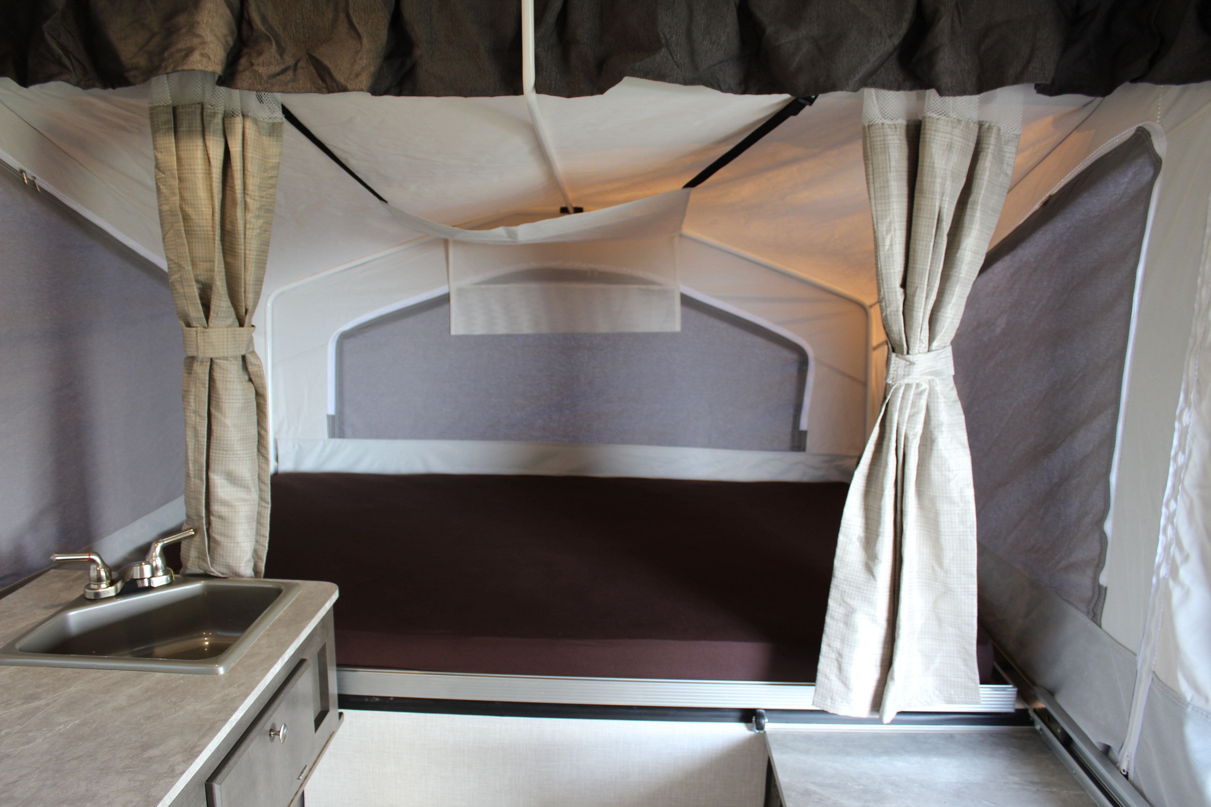 RV rental pop-up camper interior: features a bed, sink, and tied-back curtains, offering a functional camping space.. Forest River Rockwood ESP 2021